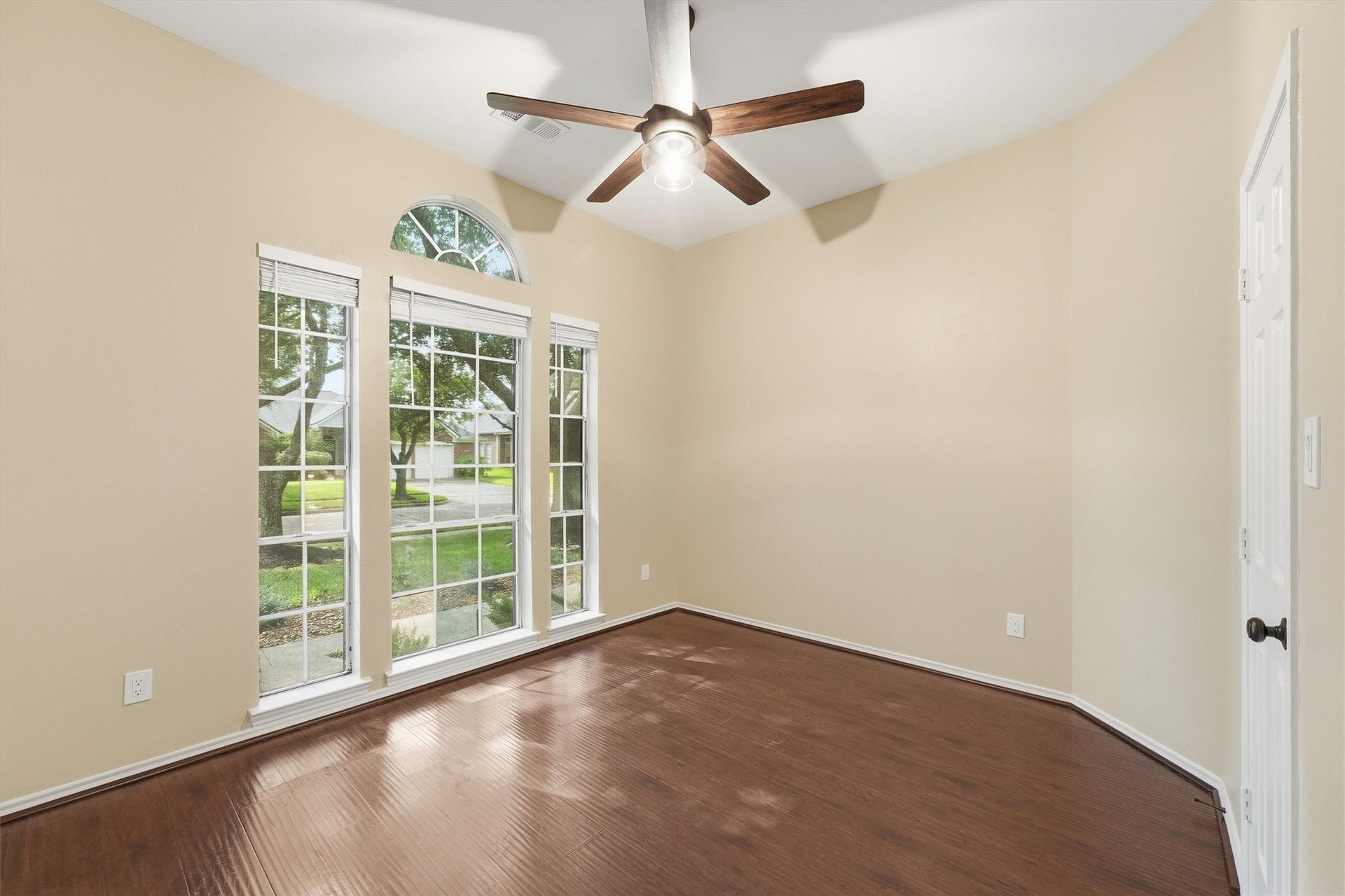Bright guest bedroom featuring a high angled ceiling line, large window for great natural light, hardwood flooring, and an updated ceiling fan.