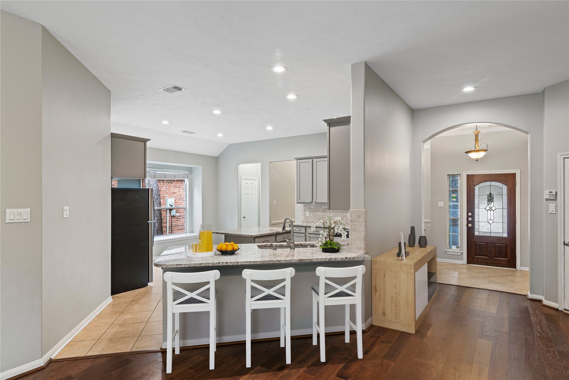 66 Bryce Branch Circle, Spring, TX 77382 Virtually Staged: Bright and inviting kitchen with granite countertops, modern appliances, and a spacious island with bar seating, seamlessly flowing into an elegant entryway with a decorative front door.