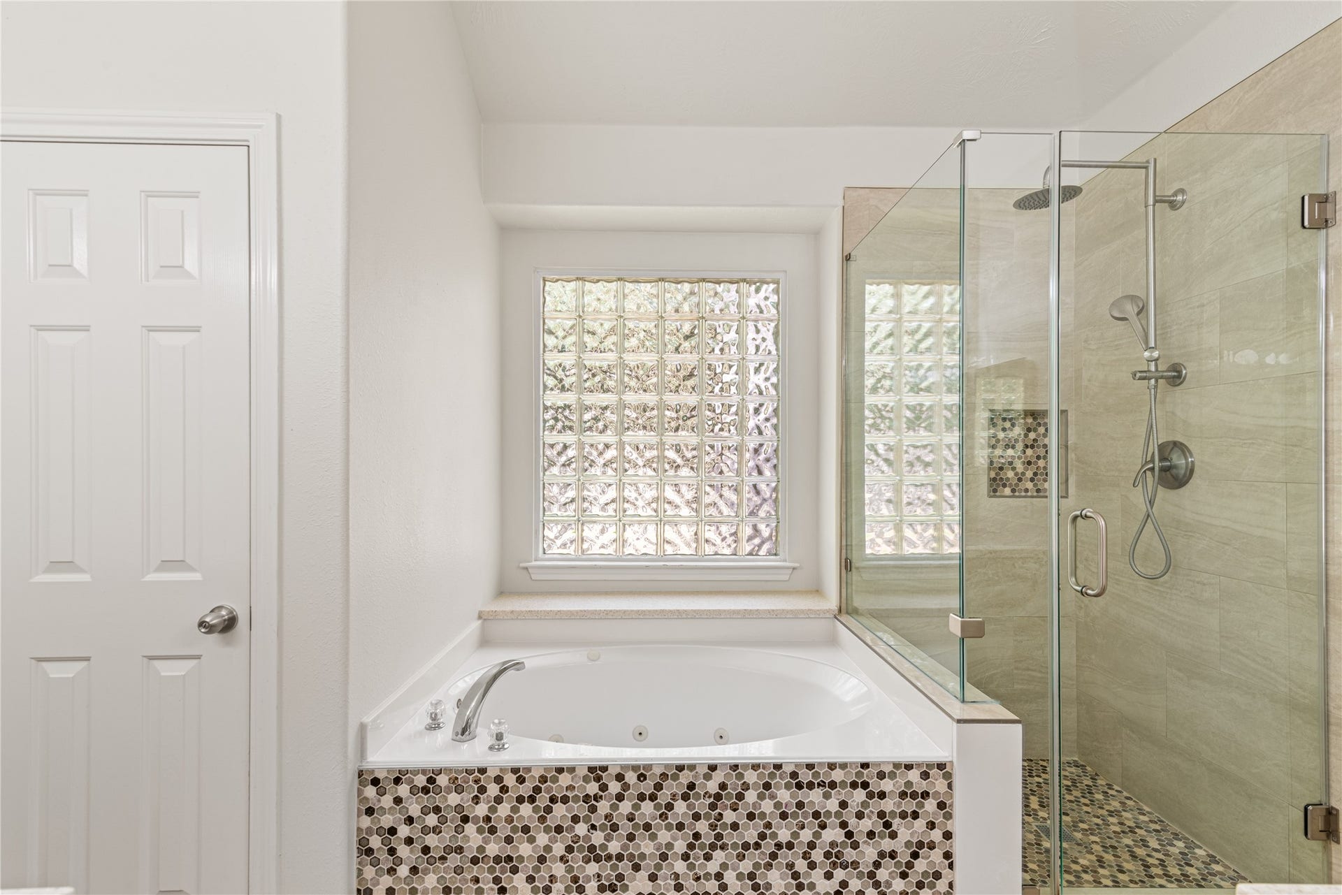 66 Bryce Branch Circle, Spring, TX 77382 Luxurious master bathroom featuring a spacious glass-enclosed shower and a sleek soaking tub with mosaic tile accents, complemented by a frosted glass window for natural light and privacy.