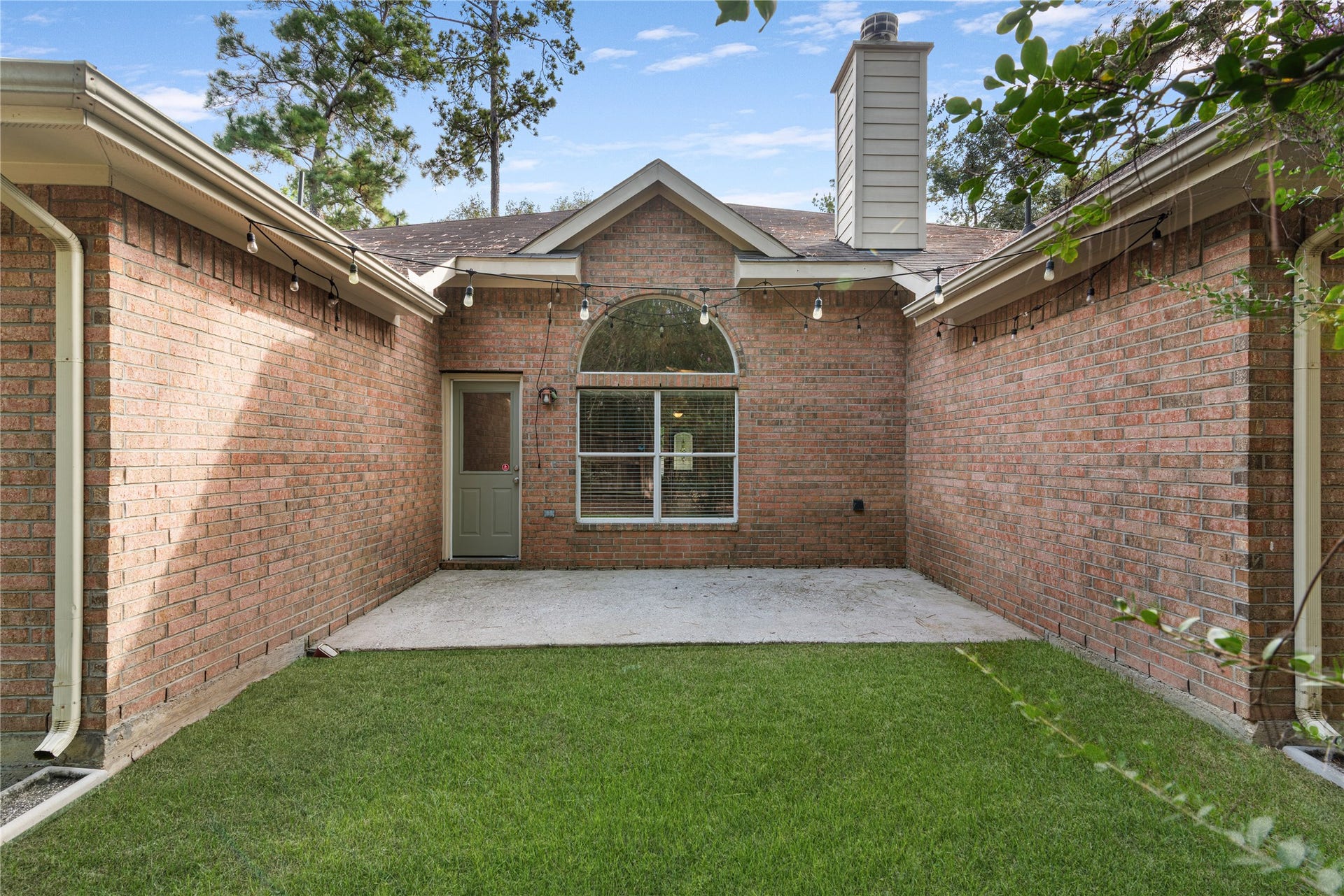 66 Bryce Branch Circle, Spring, TX 77382 Charming brick courtyard with lush green lawn, perfect for outdoor relaxation, featuring string lights for a cozy ambiance.