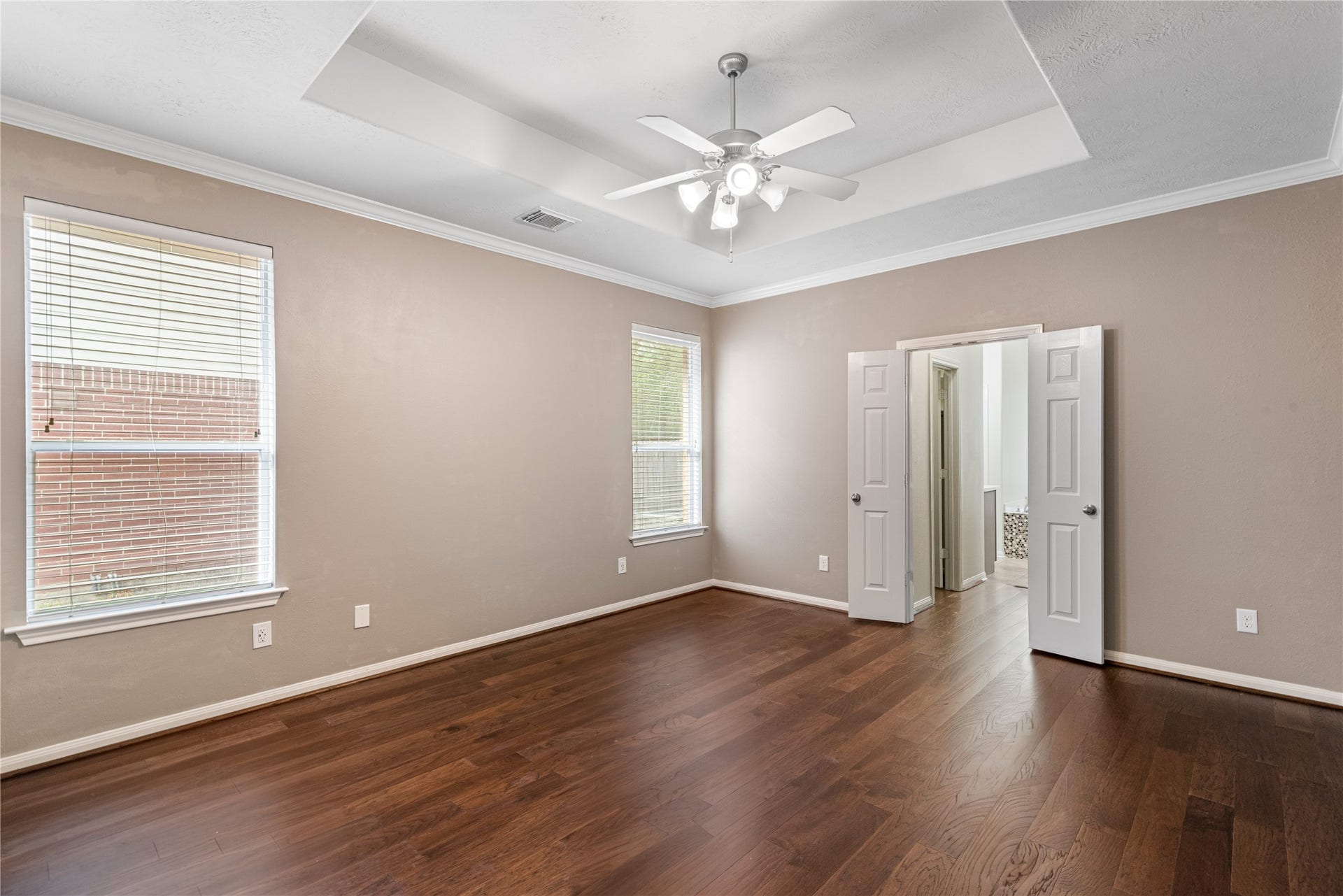 66 Bryce Branch Circle, Spring, TX 77382 Another view of the spacious master bedroom with tray ceiling and ample natural light from two large windows, leading to an ensuite bathroom through double doors.