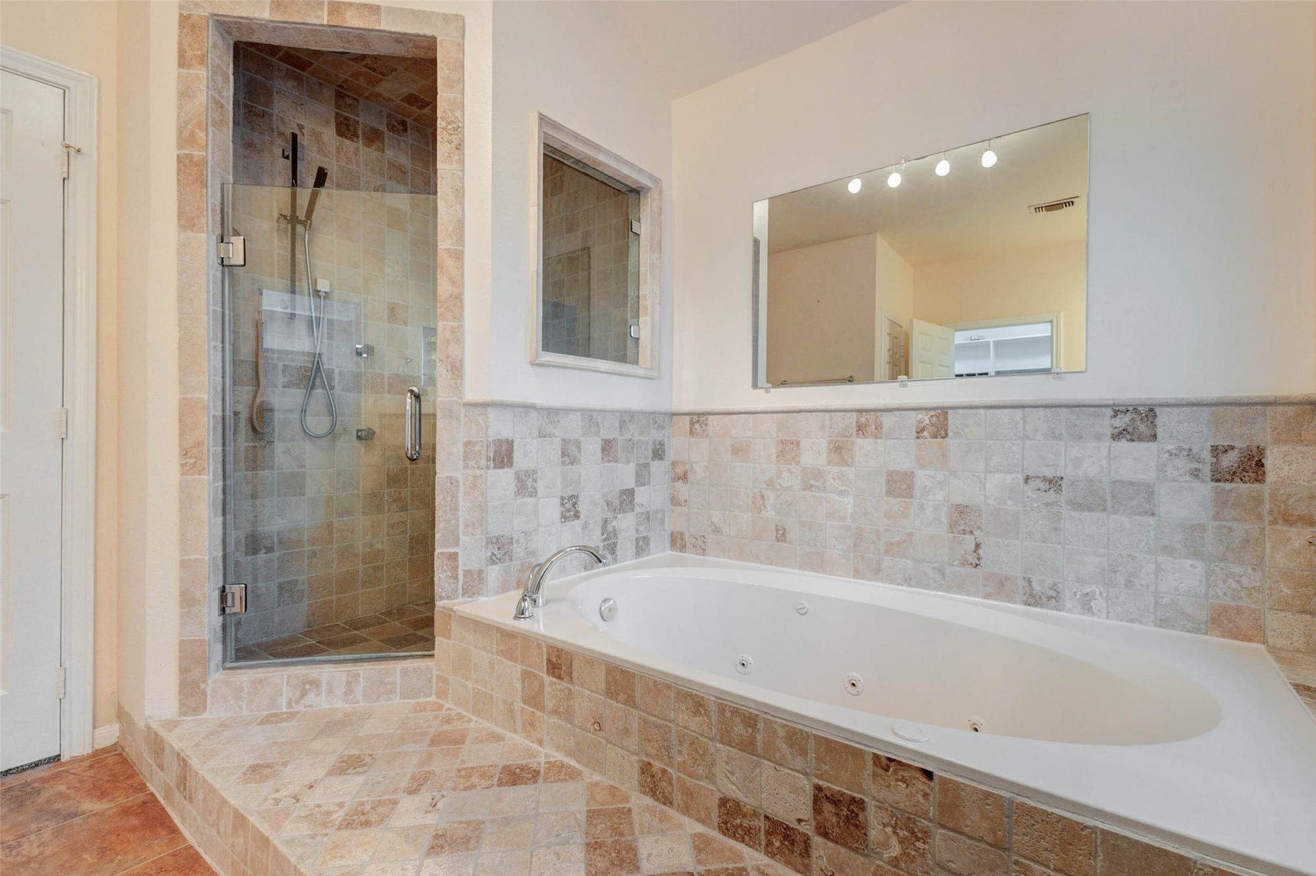 11418 Cedarwood Drive, Humble, TX 77338 A close-up of the primary bath showcases the jetted soaking tub and separate tiled shower with glass enclosure. The neutral tile surround, built-in ledge, and large mirror create a classic spa-style feel, offering a relaxing place to unwind at the end of the day while maintaining practical separation between tub and shower.