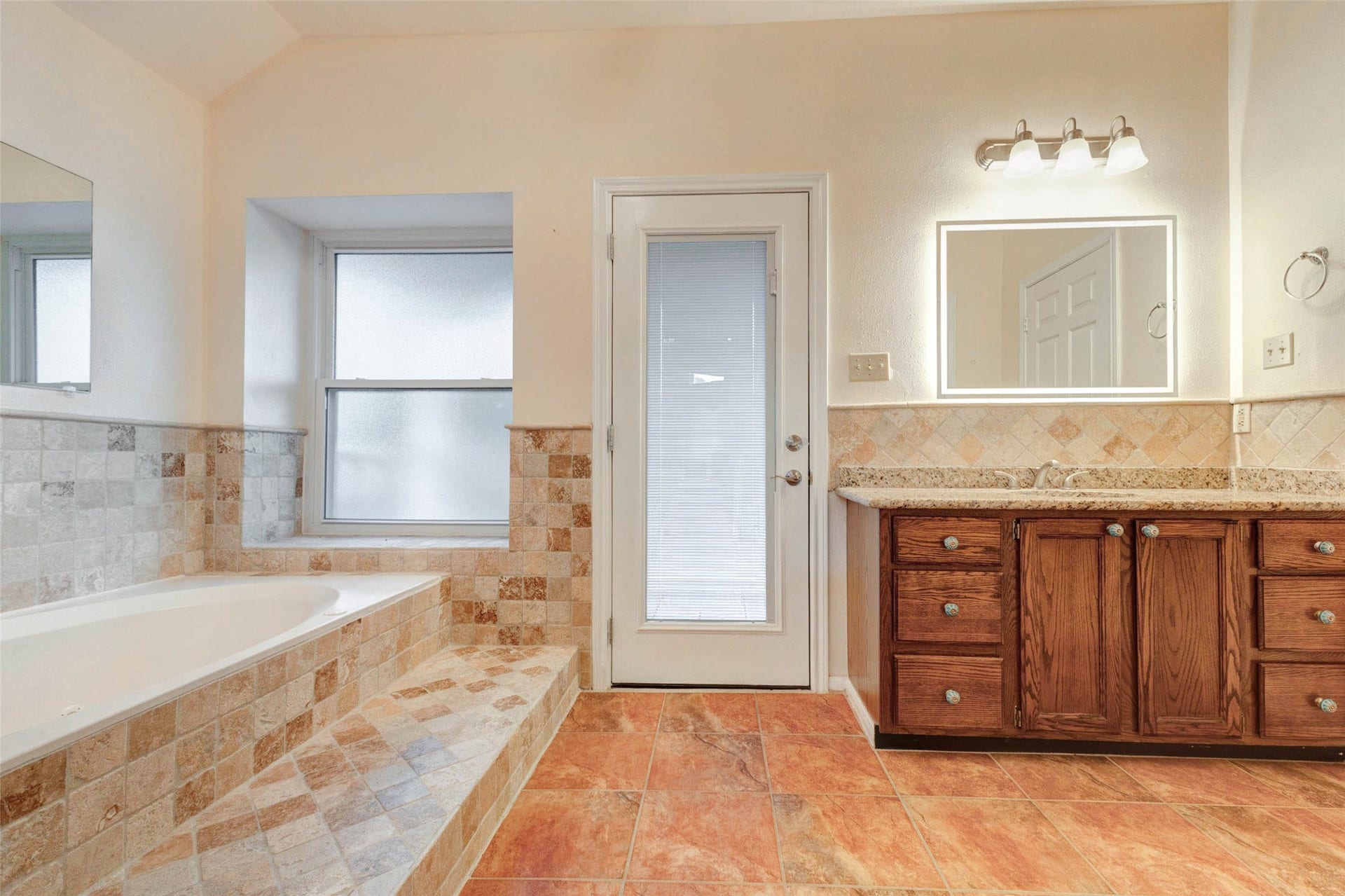 11418 Cedarwood Drive, Humble, TX 77338 The primary bath features a jetted soaking tub, tiled surround, separate vanity area, warm wood cabinetry, and direct exterior-style door access. Neutral tile finishes and generous floor space create a comfortable bath layout with room to unwind, refresh, and enjoy a private retreat connected to the upstairs living spaces.