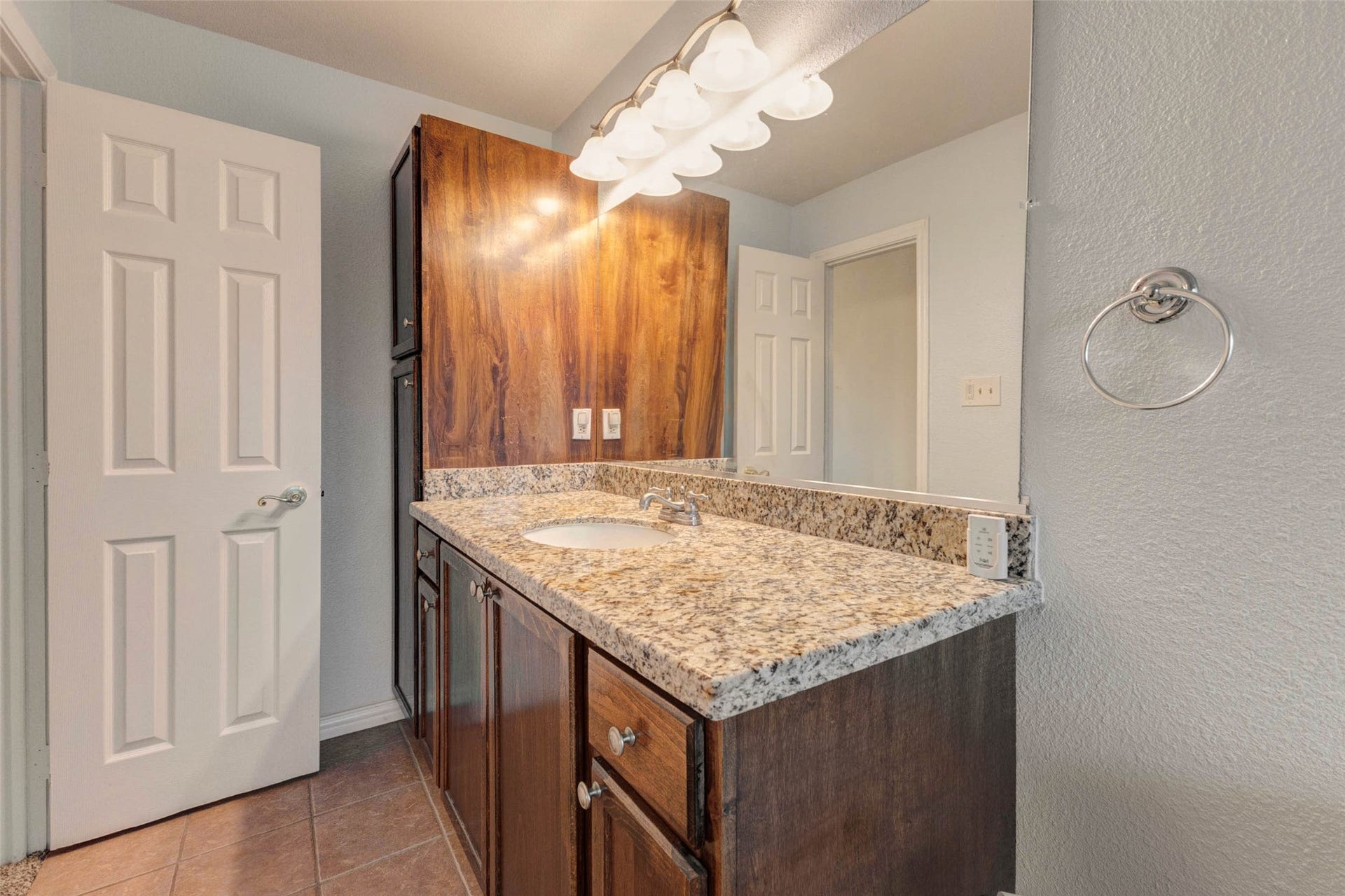 11418 Cedarwood Drive, Humble, TX 77338 This secondary bath vanity area showcases a granite-style countertop, rich wood cabinetry, wide mirror, and bright overhead lighting. Neutral wall tones and tile flooring create a clean, functional space with plenty of counter surface and storage, making daily routines simple and convenient for guests or secondary bedrooms.