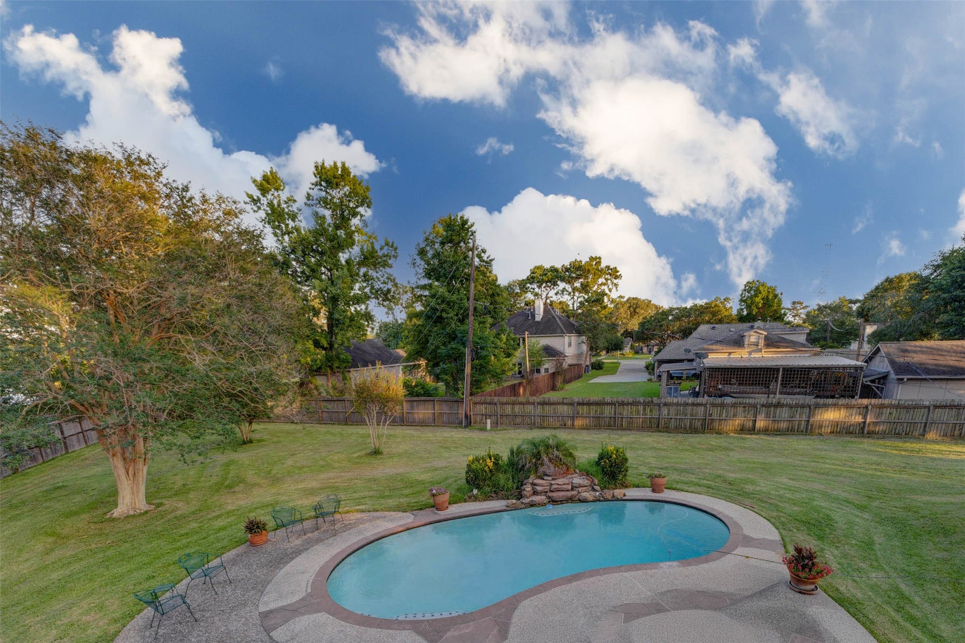11418 Cedarwood Drive, Humble, TX 77338 A wide backyard view captures the sparkling in-ground pool, expansive lawn, mature trees, and fully fenced setting beneath a bright blue sky. With generous patio space and open green areas surrounding the pool, this outdoor retreat offers room to swim, lounge, entertain, garden, play, or simply enjoy the privacy and scale of this exceptional Ramblewood lot.