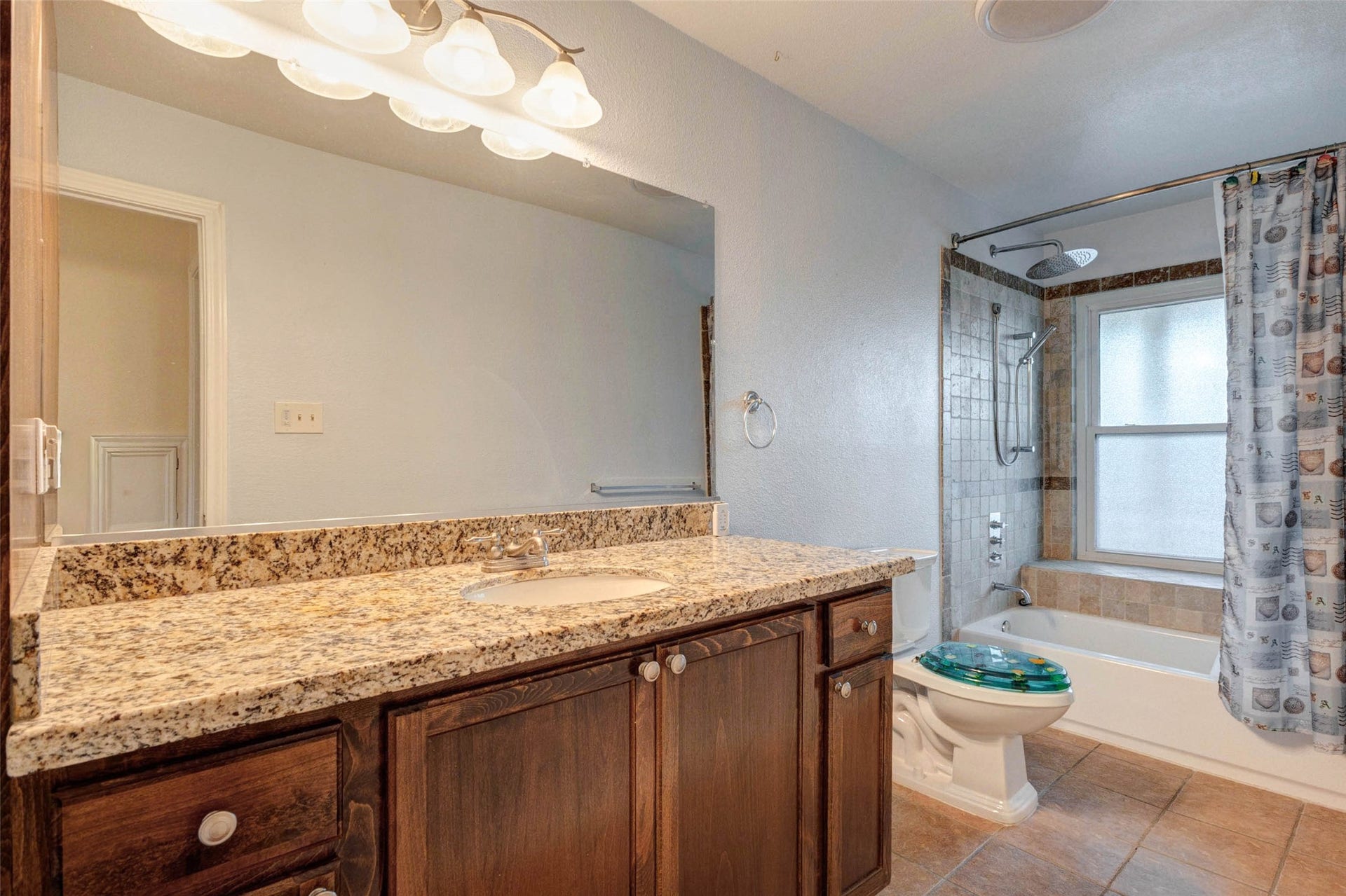 11418 Cedarwood Drive, Humble, TX 77338 The secondary bathroom features a granite-style vanity countertop, dark wood cabinetry, large mirror, updated light fixture, and a tub/shower combination with tile surround. A window brings in natural light while the functional layout offers everyday convenience for family members or guests, with practical finishes and generous counter space.