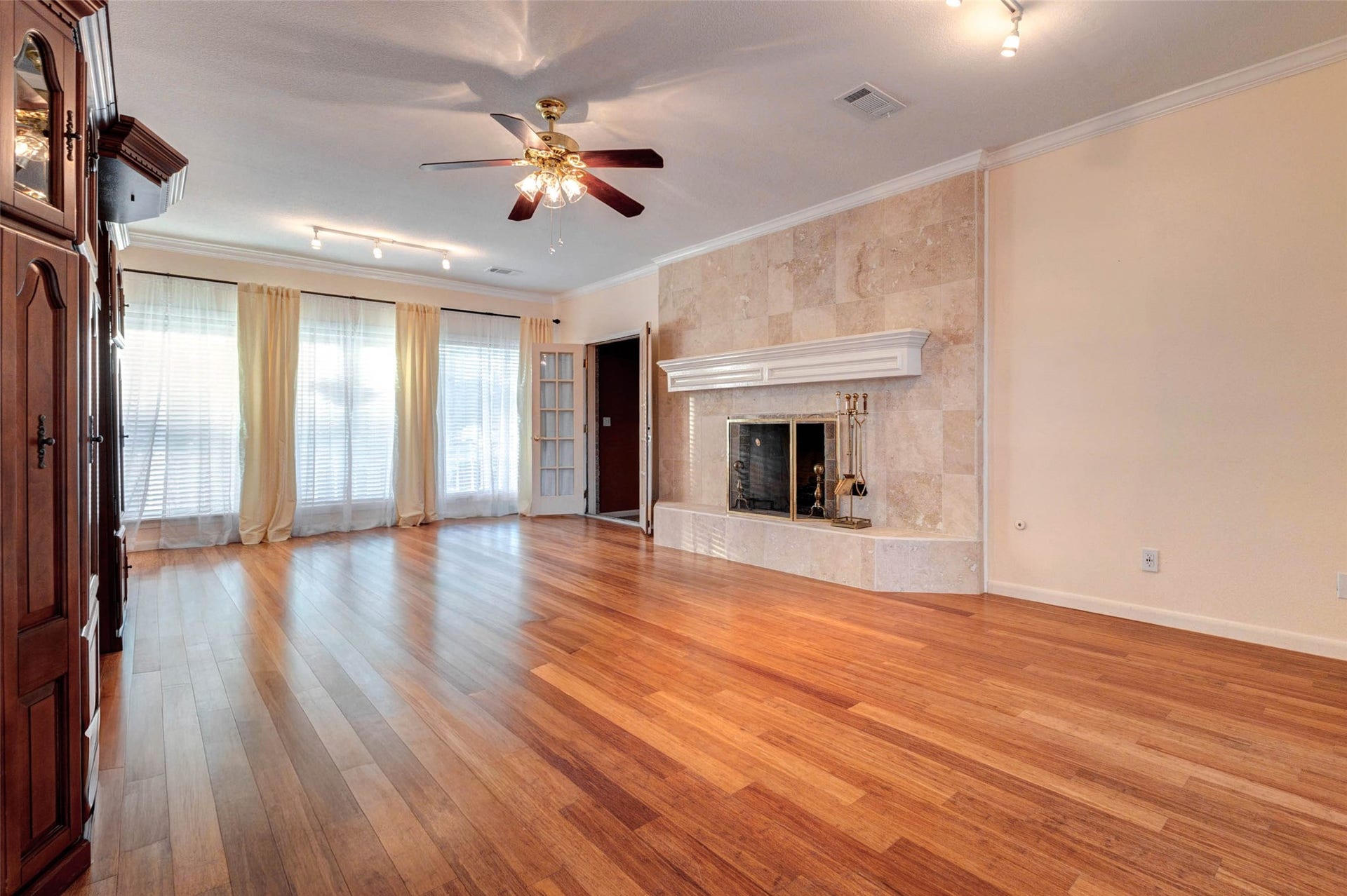 11418 Cedarwood Drive, Humble, TX 77338 A spacious main living area features warm wood-look flooring, crown molding, ceiling fan, track lighting, and a beautiful tiled fireplace with a classic mantel. Large windows bring in natural light, while the open layout offers plenty of room for seating, entertaining, and everyday gathering. The built-in cabinetry adds character and storage.