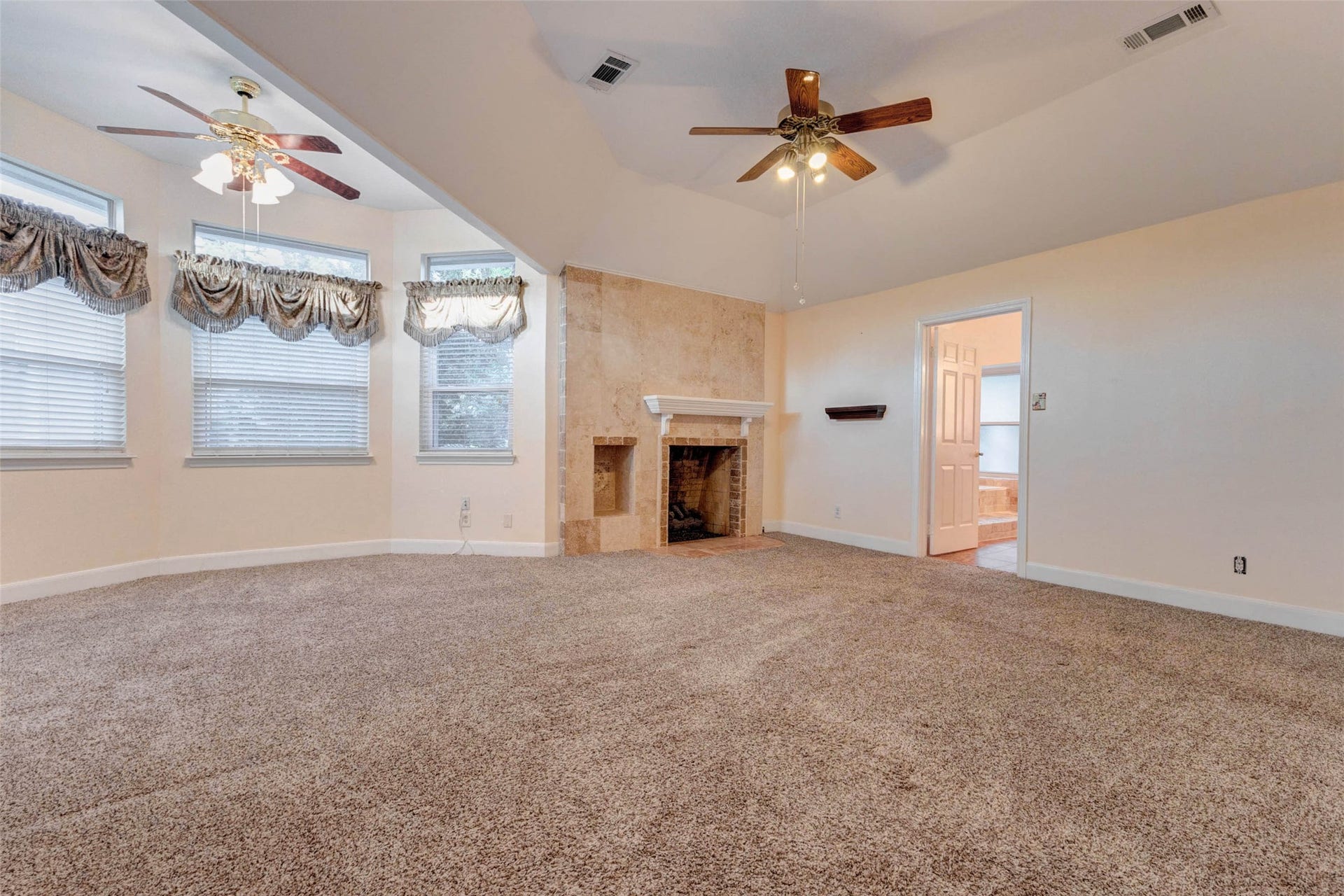 11418 Cedarwood Drive, Humble, TX 77338 The primary bedroom offers a spacious retreat with soft carpet, vaulted ceiling, dual ceiling fans, and a beautiful tiled fireplace that adds warmth and character. A curved window alcove brings in natural light and creates an inviting sitting area, while the generous layout provides room for large-scale furniture, relaxation, and a private escape within the home.