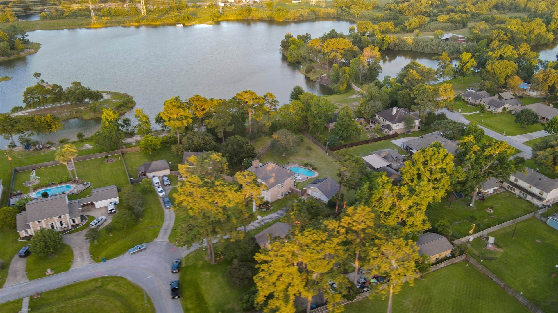 11418 Cedarwood Drive, Humble, TX 77338 An elevated aerial view showcases the homes peaceful Ramblewood setting surrounded by mature trees, neighboring estate-style lots, and scenic water views nearby. The propertys private pool, spacious yard, detached garage, and tucked-away cul-de-sac location are visible from above, highlighting the rare sense of space, privacy, and natural beauty this Humble property offers.