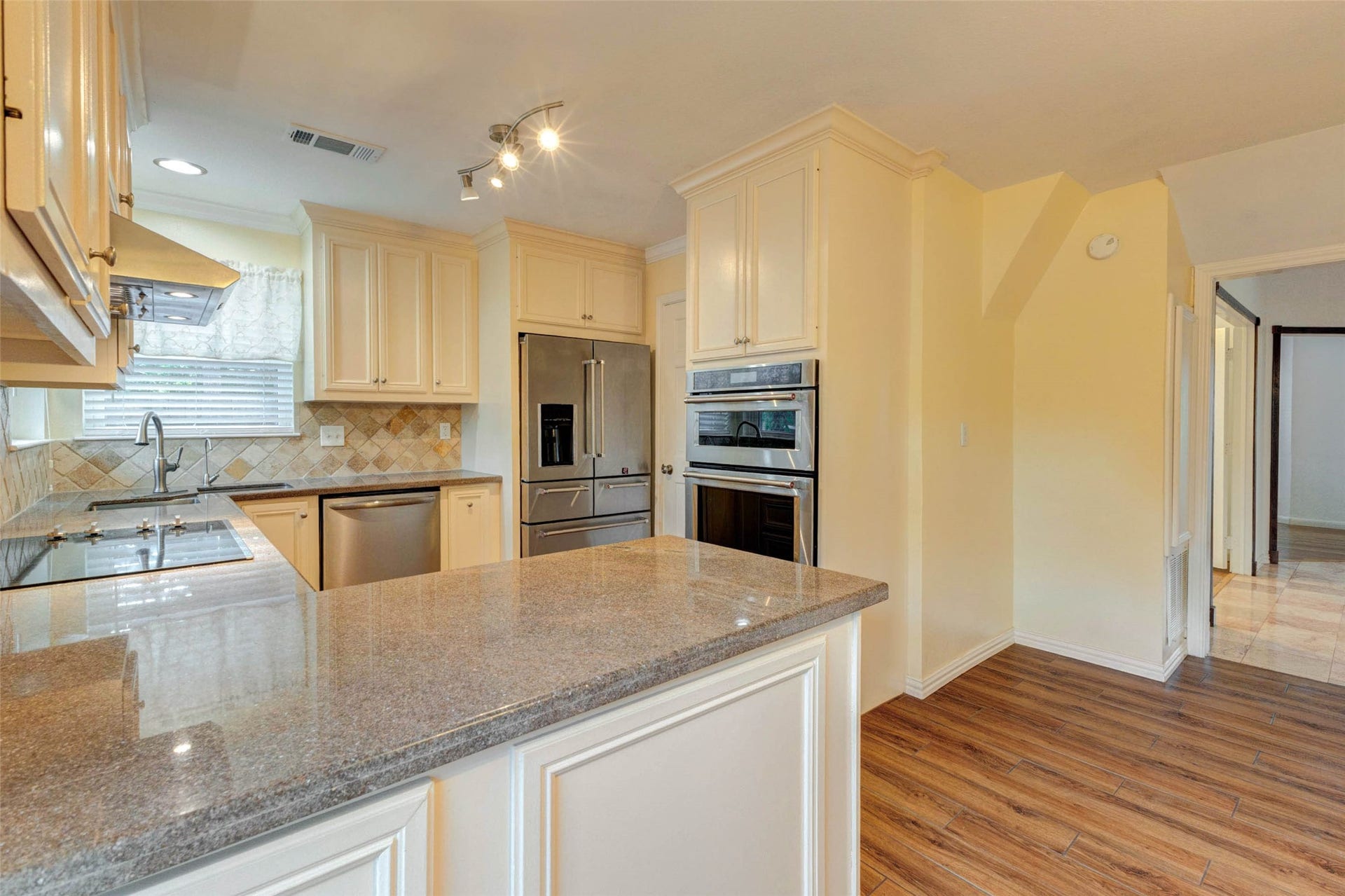 11418 Cedarwood Drive, Humble, TX 77338 This kitchen view highlights the spacious counter surfaces, cream cabinetry, stainless appliances, built-in oven and microwave, electric cooktop, tile backsplash, and warm wood-look flooring. The layout provides plenty of prep space and storage while maintaining easy access to the breakfast area and adjoining living spaces.