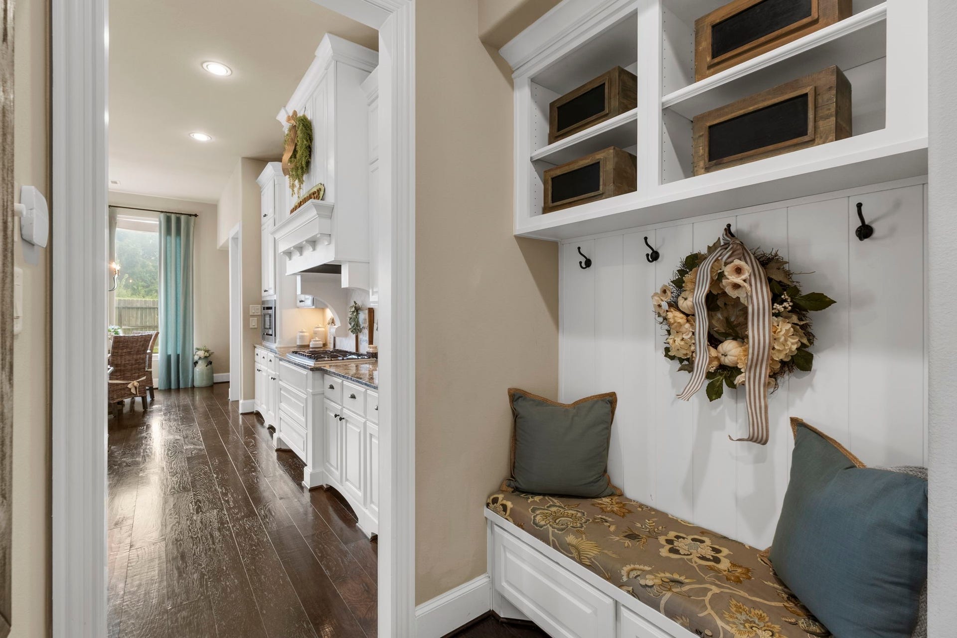 34 Stefano Way, Missouri City, TX 77459 Custom built-in mudroom entry nook featuring beadboard accent paneling, storage coat hooks, upper display cubbies, and a fitted bench with built-in lower drawers. Hallway beyond leads directly into the main kitchen area.