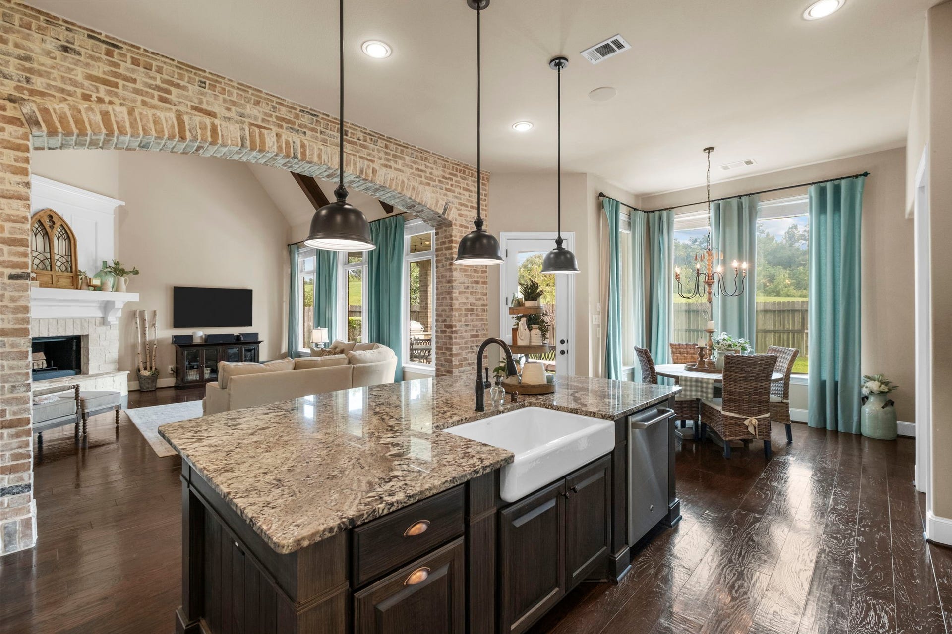 34 Stefano Way, Missouri City, TX 77459 View from the kitchen island featuring an apron-front farmhouse sink with a gooseneck faucet and built-in dishwasher. Showcases the dramatic exposed brick archway separating the kitchen from the living area, along with the adjacent casual breakfast nook.