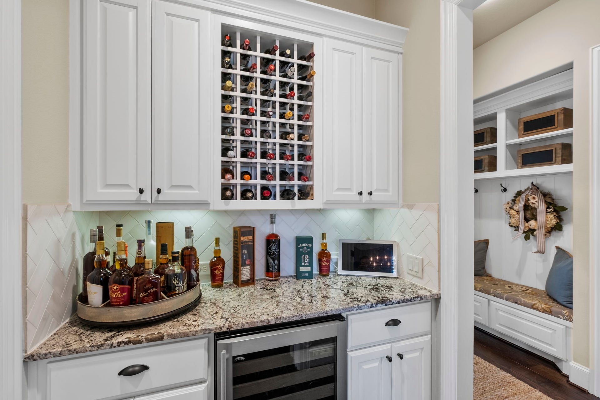 34 Stefano Way, Missouri City, TX 77459 Dedicated built-in dry bar area boasting a custom white cabinet surround, integrated built-in wine rack lattice, granite countertop, herringbone tile backsplash, under-cabinet lighting, and space for a beverage cooler.