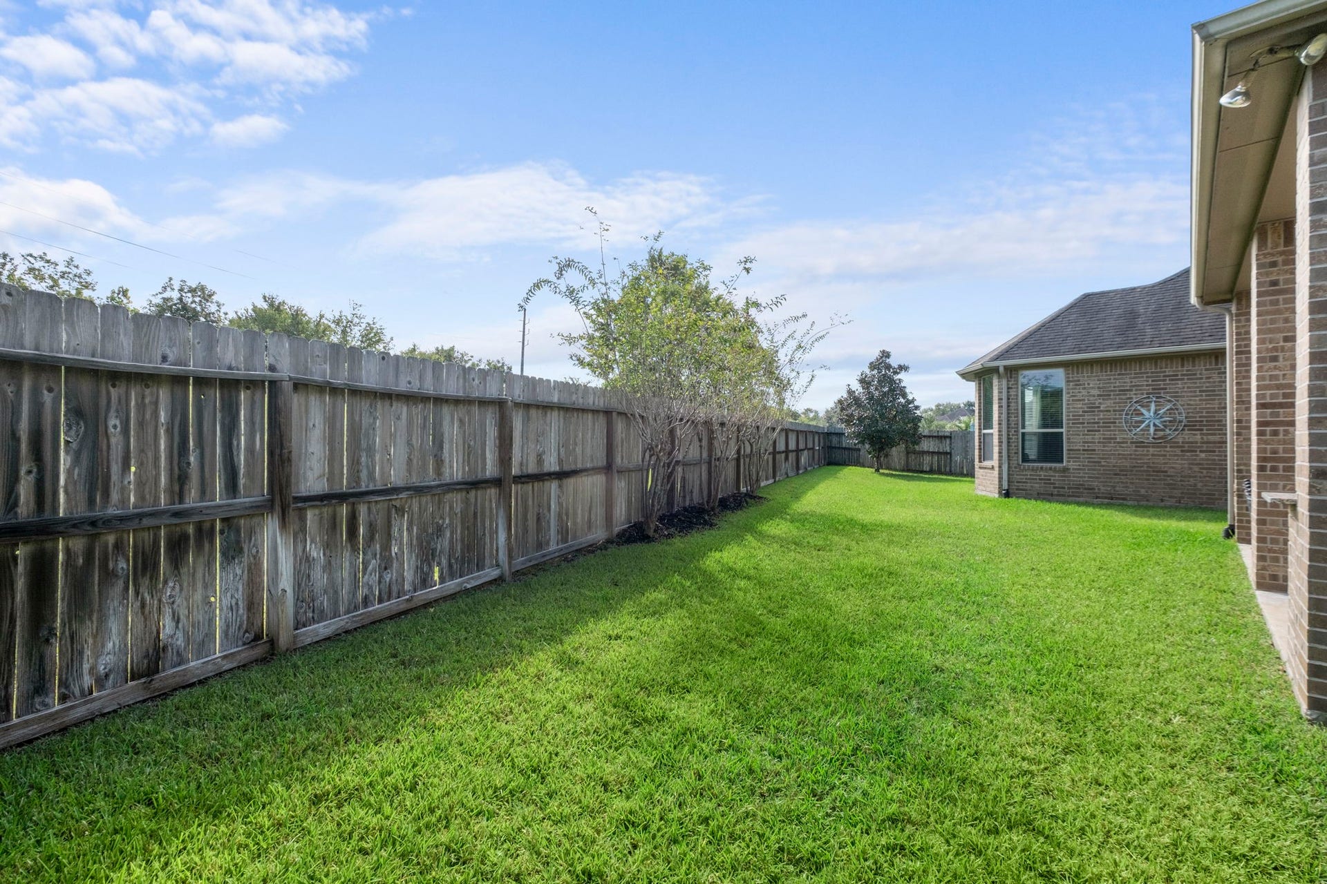 34 Stefano Way, Missouri City, TX 77459 Expansive side yard featuring lush green lawn and an extensive wood privacy fence with mature boundary plantings running along the property line.