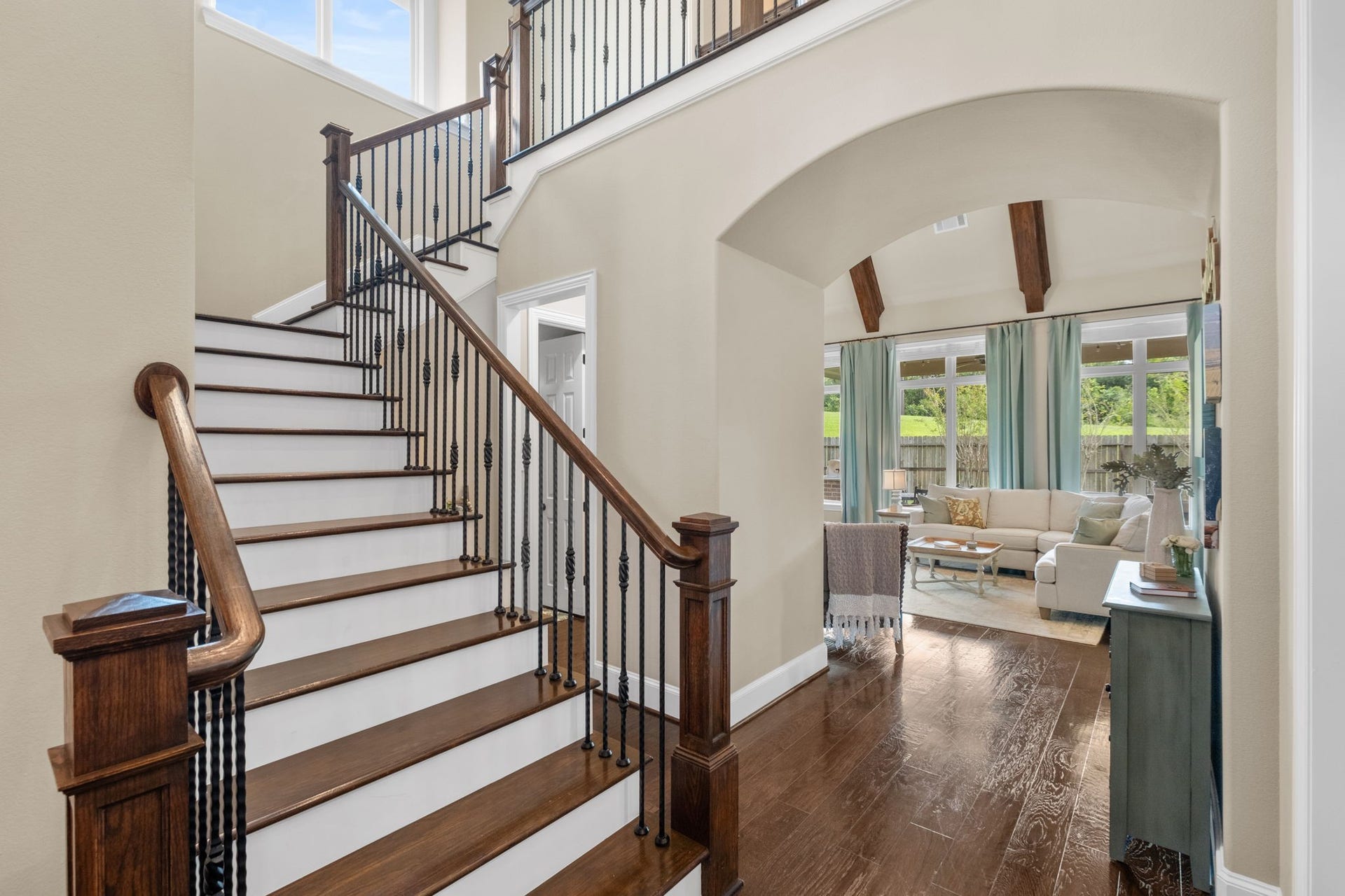 34 Stefano Way, Missouri City, TX 77459 Dramatic entry stairwell featuring rich hardwood treads, painted white risers, and a wrought-iron decorative balustrade. An elegant architectural archway opens into the main living room, highlighting the home's open-concept layout and continuous hardwood flooring.