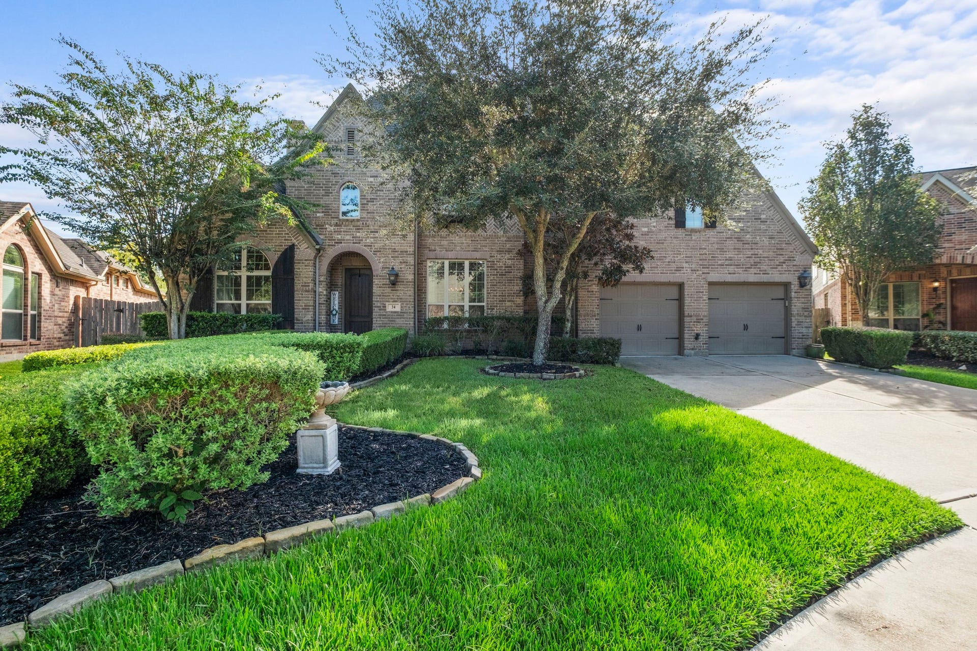 34 Stefano Way, Missouri City, TX 77459 Expansive front lawn highlighting professional landscaping with sculpted boxwood hedges, mature shade trees, and a decorative stone fountain centerpiece set in black mulch beds.