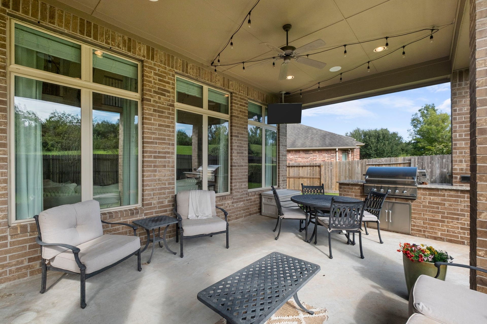 34 Stefano Way, Missouri City, TX 77459 Full view of the covered patio area showing floor-to-ceiling multi-panel rear windows and glass doors providing seamless indoor-outdoor sightlines. Features a built-in stainless steel BBQ grill with granite counter space and a brick base.