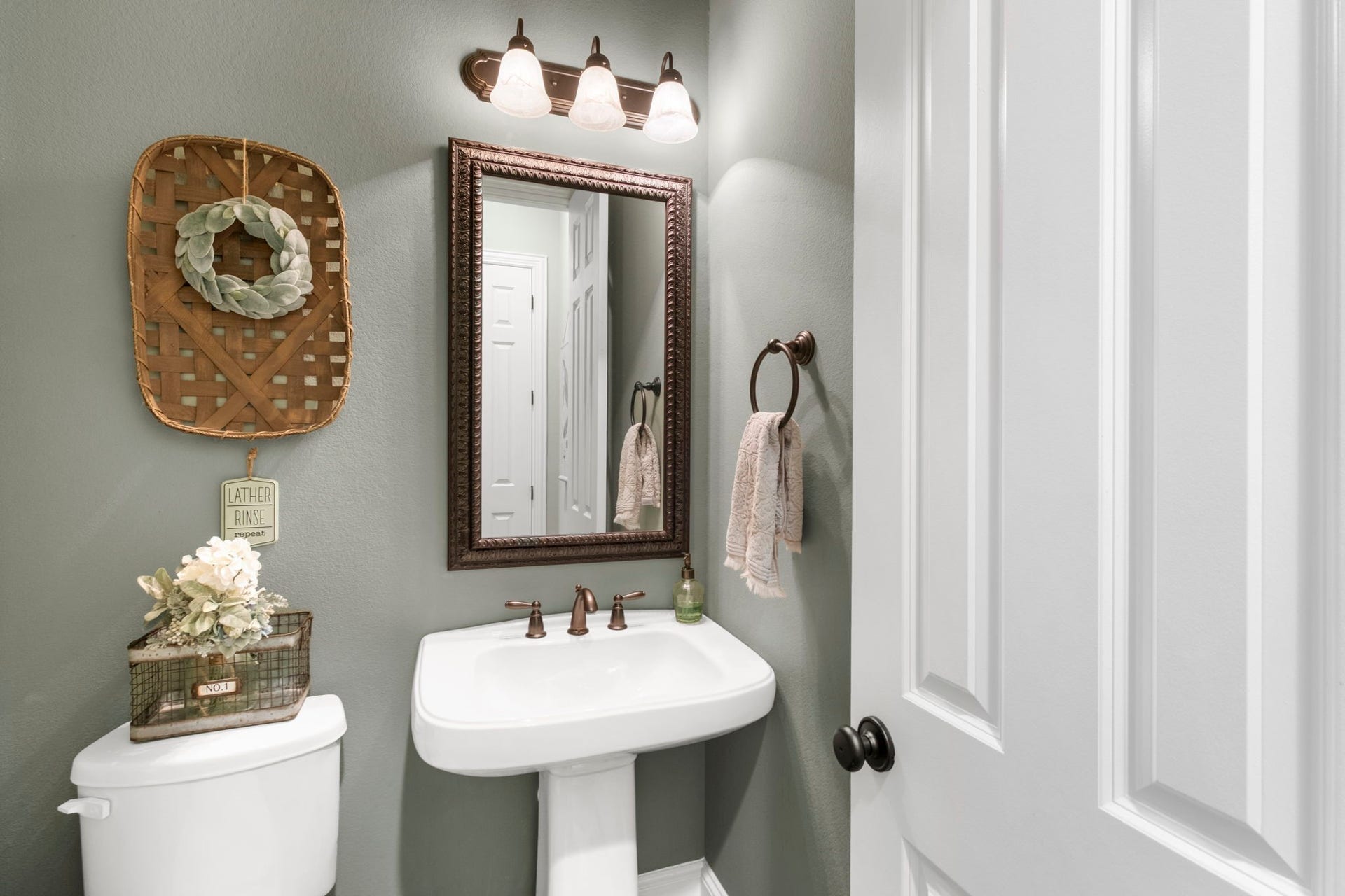 34 Stefano Way, Missouri City, TX 77459 Charming half-bath featuring a classic white porcelain pedestal sink with bronze fixtures, oil-rubbed bronze vanity lighting, decorative framed mirror, neutral sage green walls, and tile flooring.