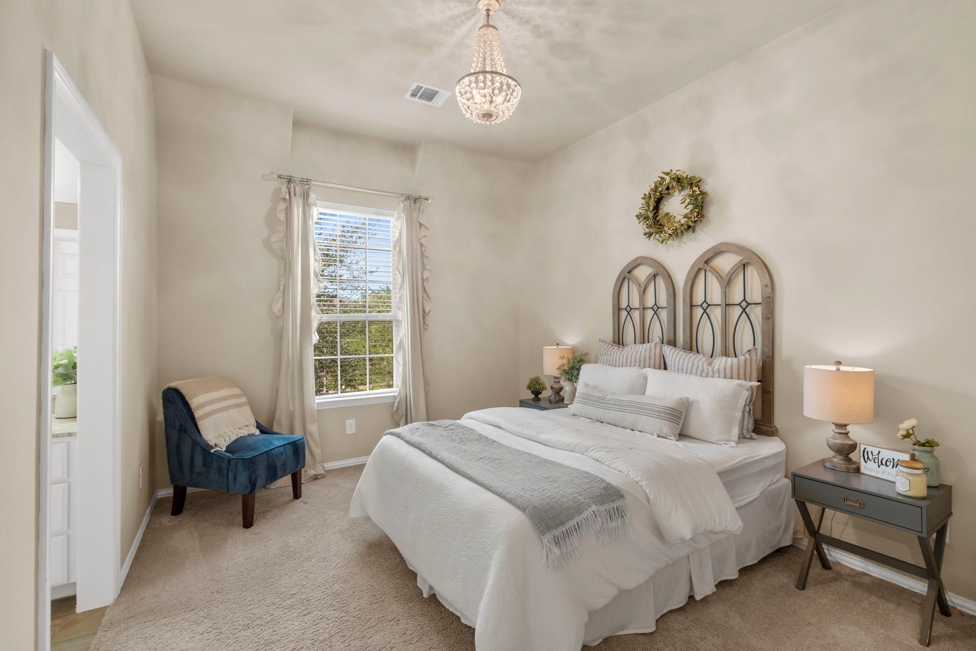 34 Stefano Way, Missouri City, TX 77459 Sunlit guest bedroom featuring plush carpeting, a vaulted ceiling line, an elegant crystal chandelier light fixture, neutral walls, and a large window overlooking the outdoor grounds. Direct access leads to an adjacent bathroom.