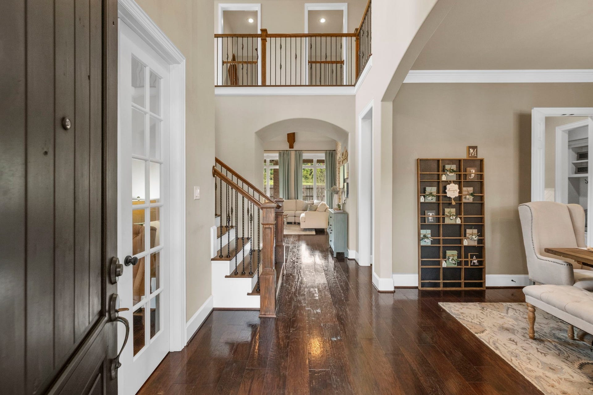 34 Stefano Way, Missouri City, TX 77459 Grand two-story foyer entry featuring warm hardwood flooring, a sweeping staircase with wrought-iron spindles, recessed lighting, and an upper-level overlook balcony. Archway leads toward the light-filled main living space.