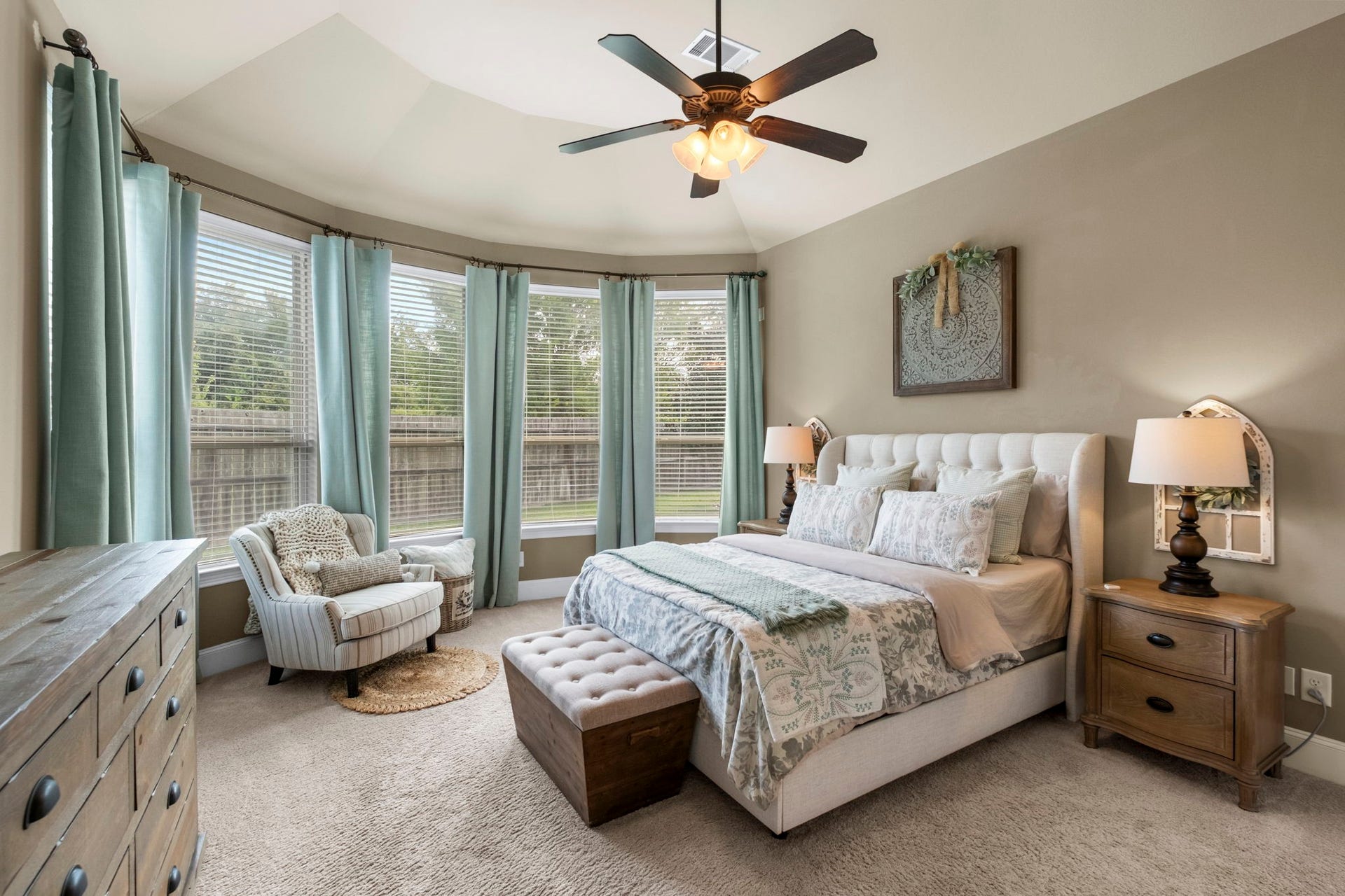 34 Stefano Way, Missouri City, TX 77459 Spacious primary suite featuring plush carpeting, a tray ceiling with a integrated ceiling fan/light fixture, and a curved bay window alcove with custom drapery overlooking the backyard.