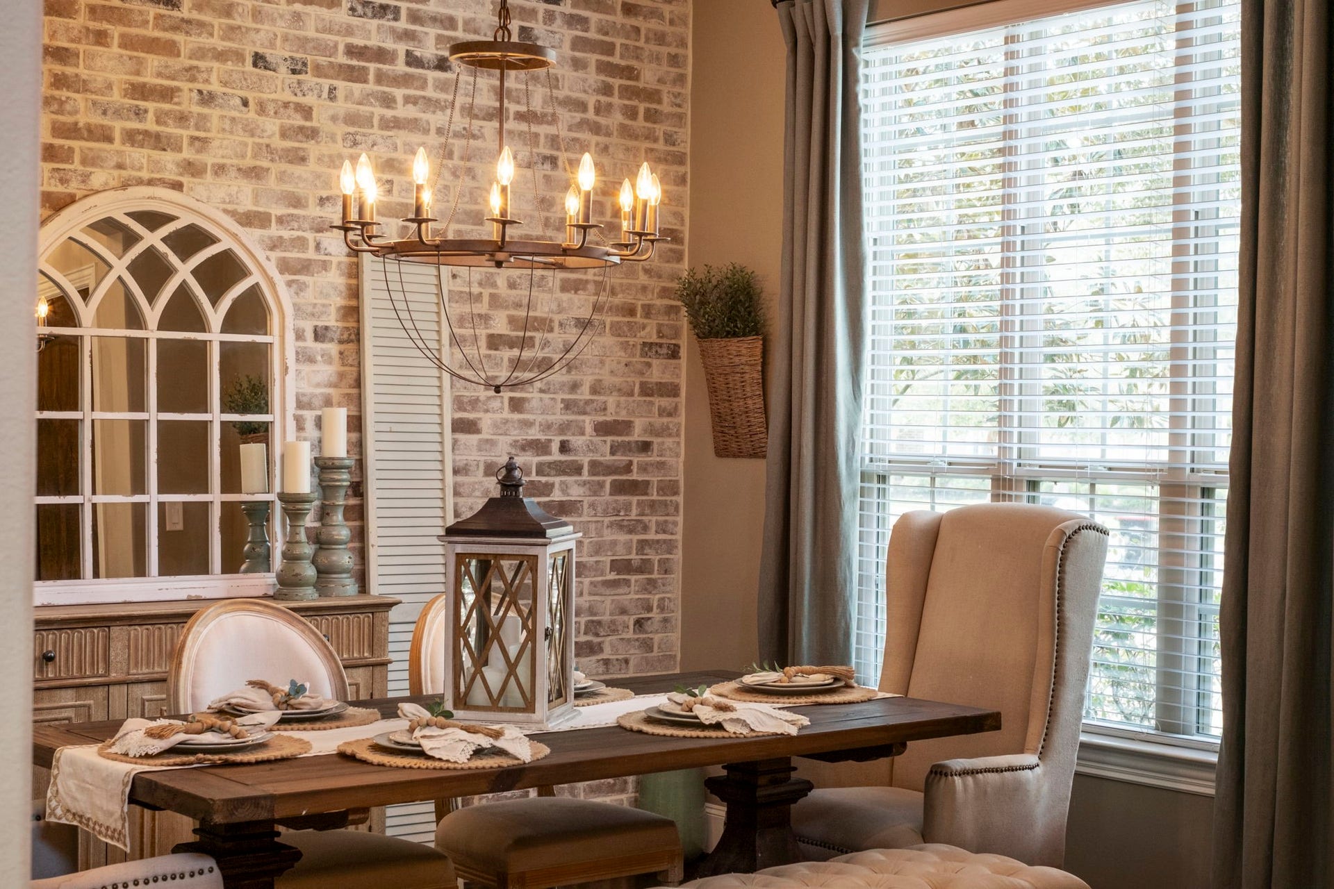 34 Stefano Way, Missouri City, TX 77459 Detailed perspective of the formal dining space highlighting the rustic exposed-brick accent wall, traditional crown molding, dark hardwood floor, and a metal wagon-wheel chandelier. Features a wide double-hung window equipped with trim moulding and blinds.