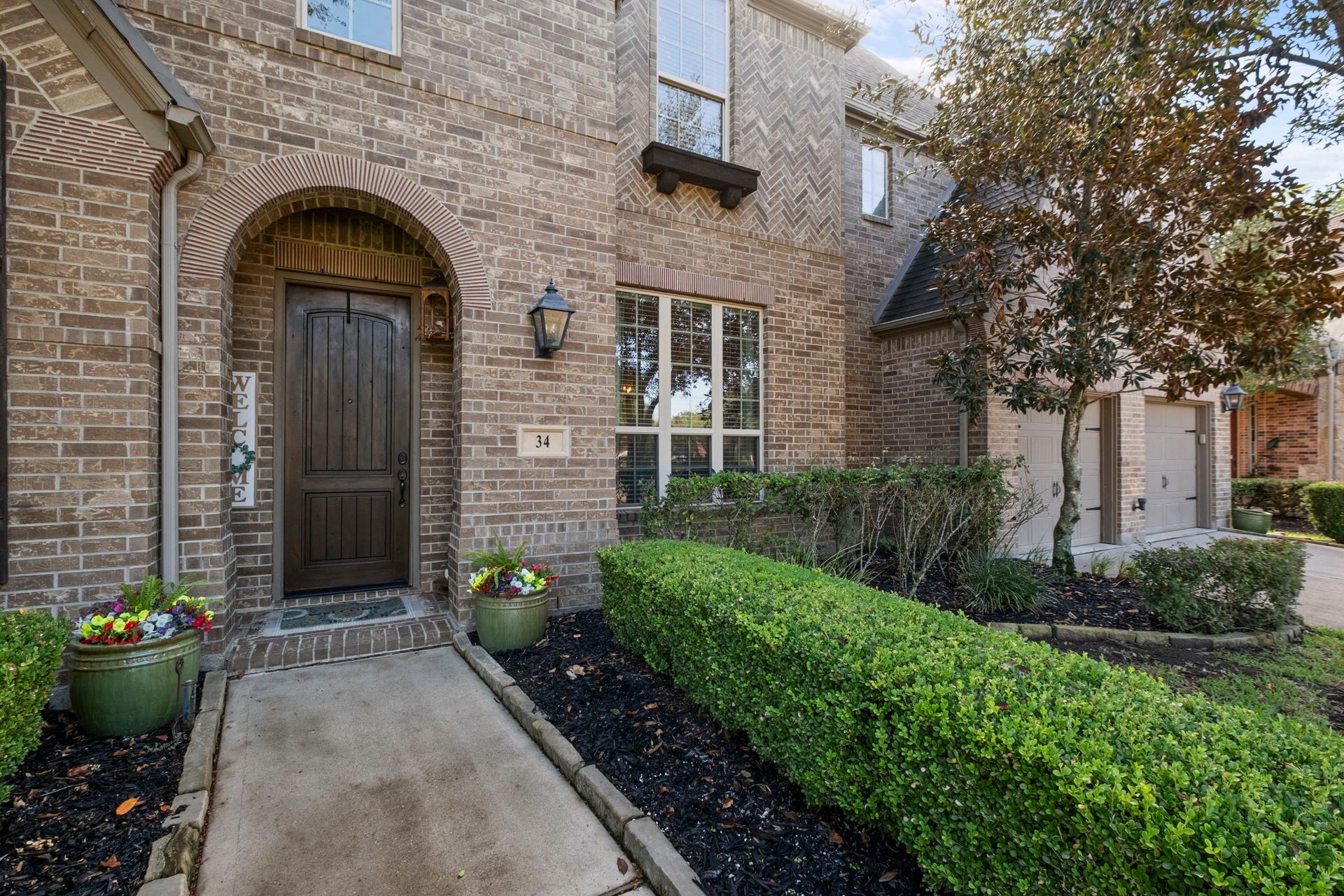 34 Stefano Way, Missouri City, TX 77459 Covered stone entry archway boasting a custom solid wood front door with a glass accent window. Detailed with brick herringbone accents, a charming window flower box, and custom stone address plaque.