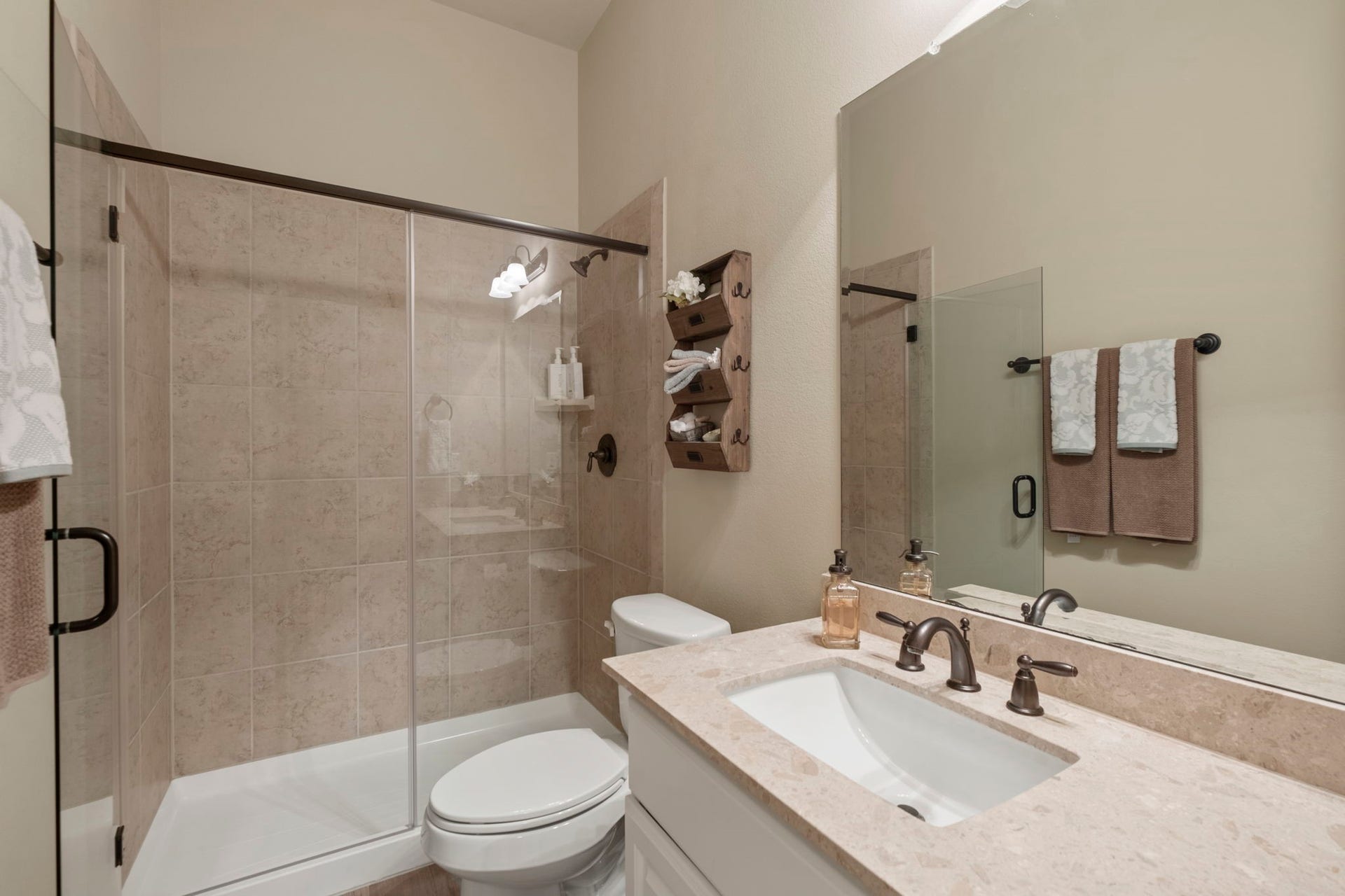 34 Stefano Way, Missouri City, TX 77459 Guest bathroom featuring a neutral tile-surround walk-in shower with a frameless glass sliding door, oil-rubbed bronze fixtures, a toilet, a single-sink vanity with light marble/granite countertops, and a full-width mirror.