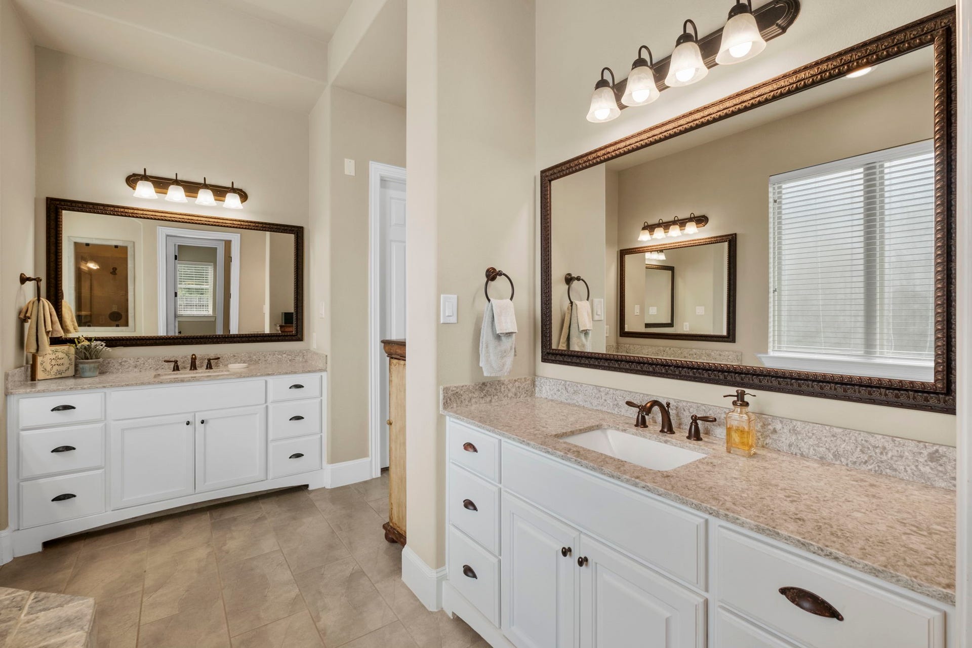 34 Stefano Way, Missouri City, TX 77459 Luxurious primary ensuite featuring dual separated white vanities with granite countertops, oil-rubbed bronze hardware, framed mirrors, updated vanity lights, and neutral tile flooring.
