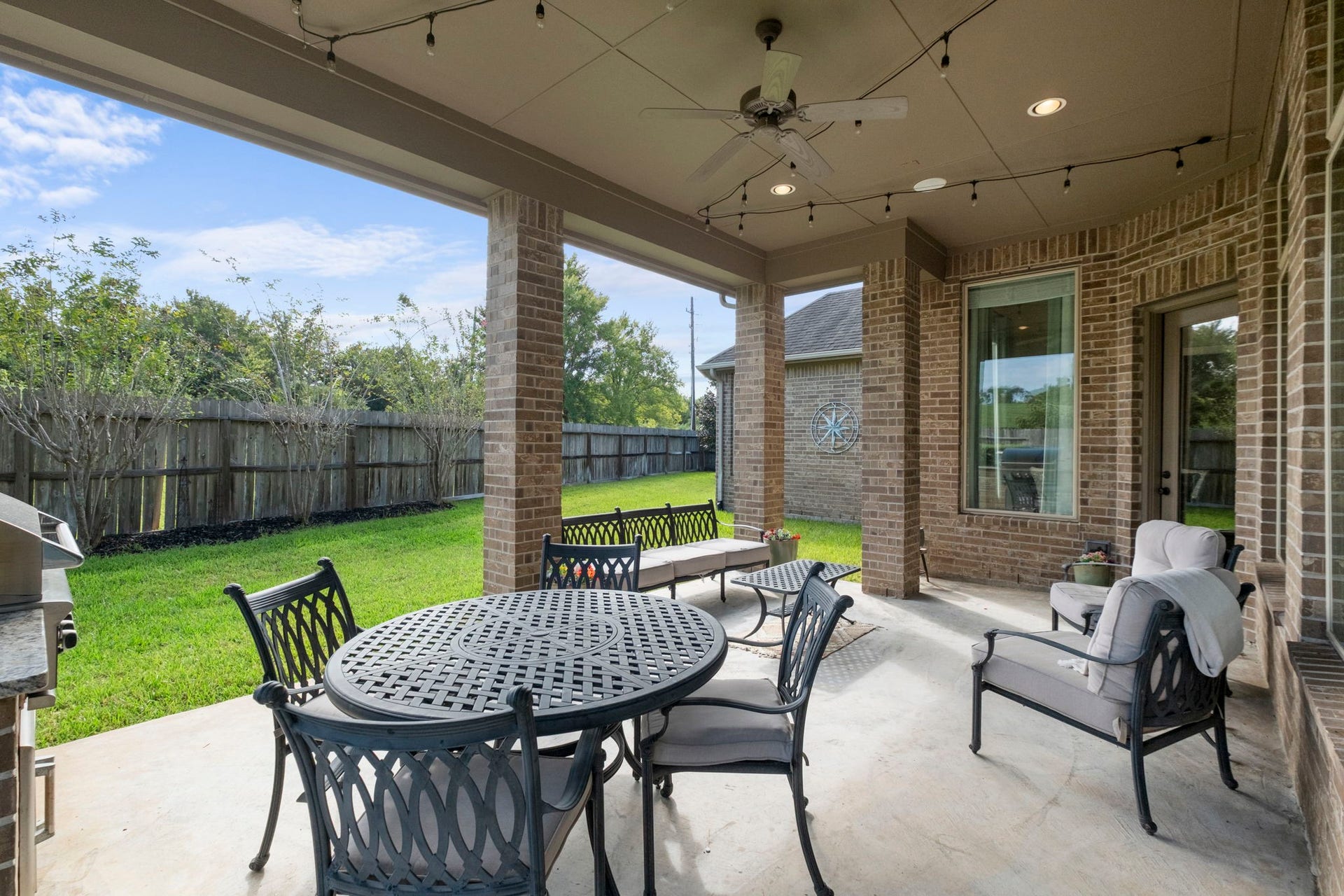 34 Stefano Way, Missouri City, TX 77459 Extended covered patio view highlighting the high-volume ceiling, brick support columns, and concrete deck flooring overlooking the fully fenced green backyard.