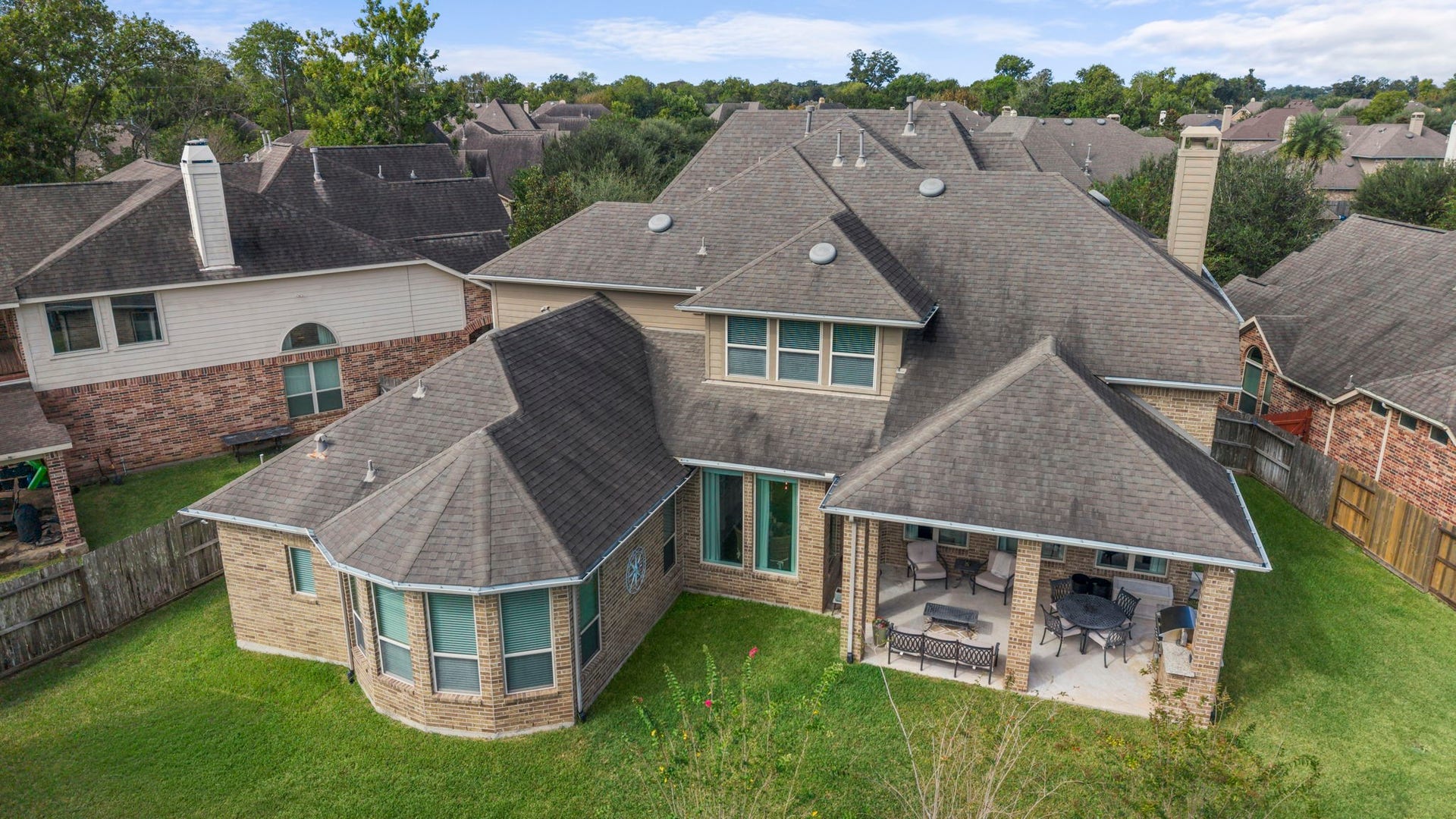 34 Stefano Way, Missouri City, TX 77459 Low-altitude aerial view looking down at the rear of the home, featuring the covered patio, outdoor kitchen area, bay window architectural line, roof dormers, and expansive lawn.