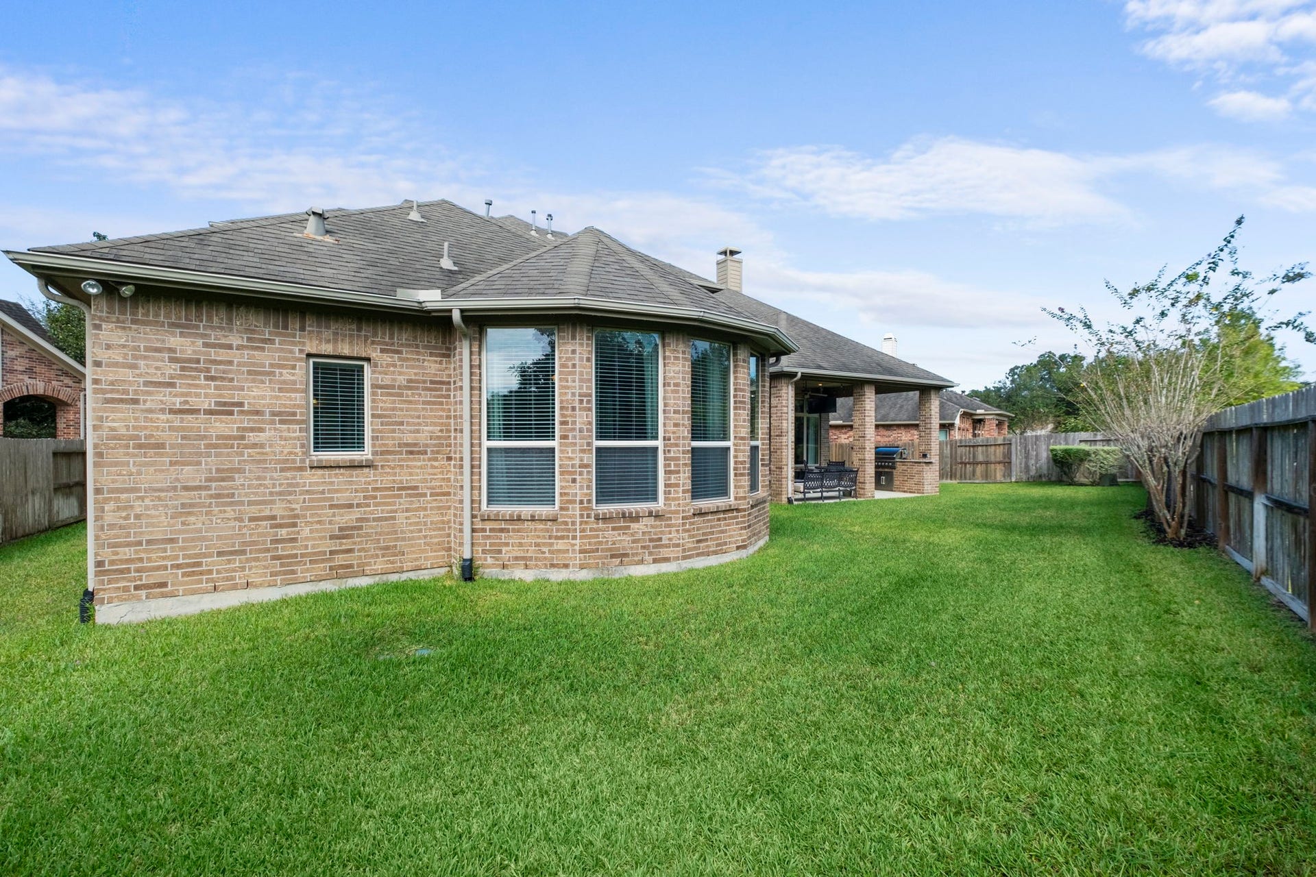 34 Stefano Way, Missouri City, TX 77459 Rear perspective showcasing the architectural brick exterior with a prominent multi-window bay bump-out, gutters, and expansive green lawn enclosed by a wood privacy fence.