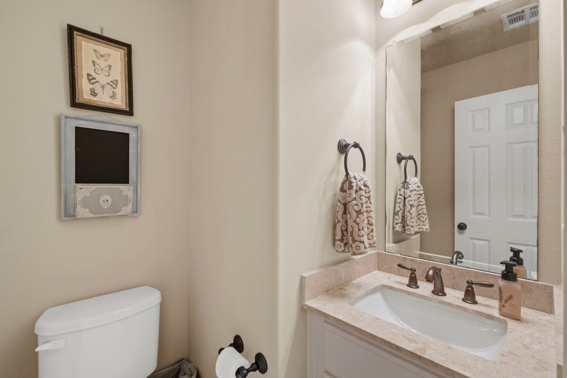 34 Stefano Way, Missouri City, TX 77459 Upstairs guest half-bath featuring a vanity with a light stone countertop, oil-rubbed bronze faucet and hardware, large frameless wall mirror, neutral wall paint, and toilet alcove.