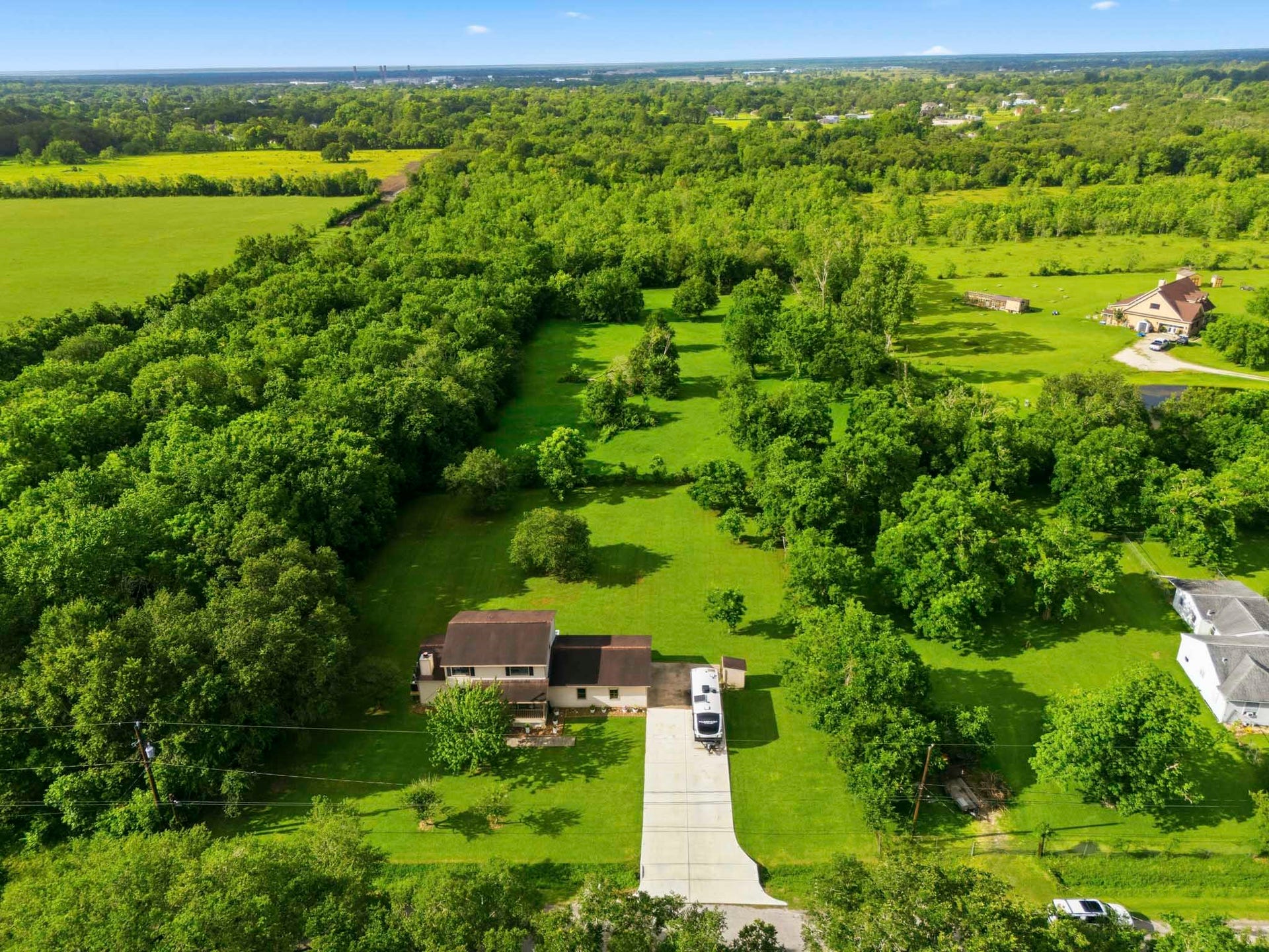 This photo showcases a spacious rural property surrounded by lush greenery and mature trees, providing ample privacy. The long double driveway leads to a cozy home, ideal for those seeking tranquility and a connection with nature.