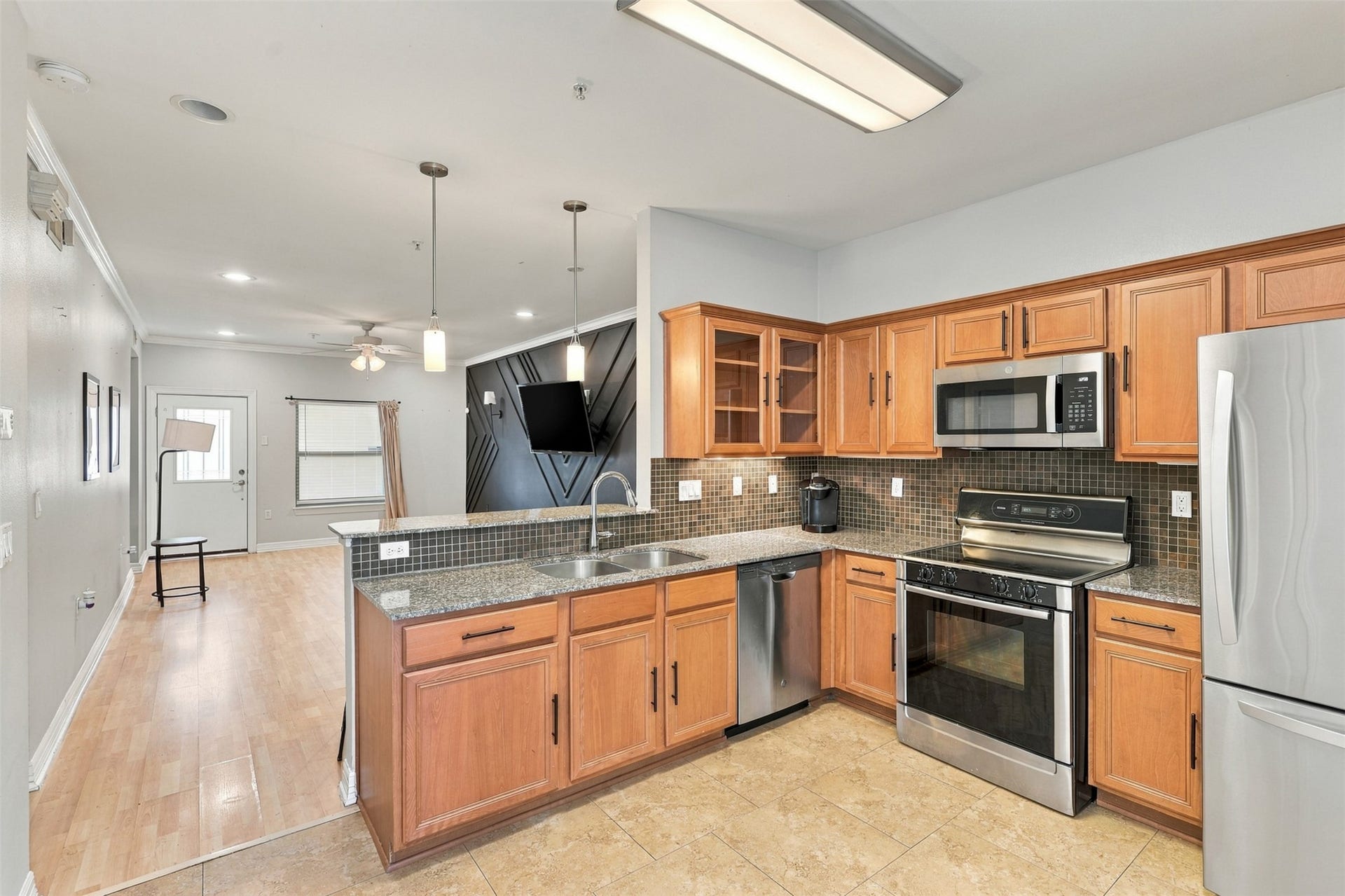 3501 Chenevert Street, #3, Houston, TX 77004 Modern kitchen with stainless steel appliances, elegant wood cabinetry, and stylish tile backsplash, seamlessly connecting to an open living area with hardwood floors and contemporary lighting.