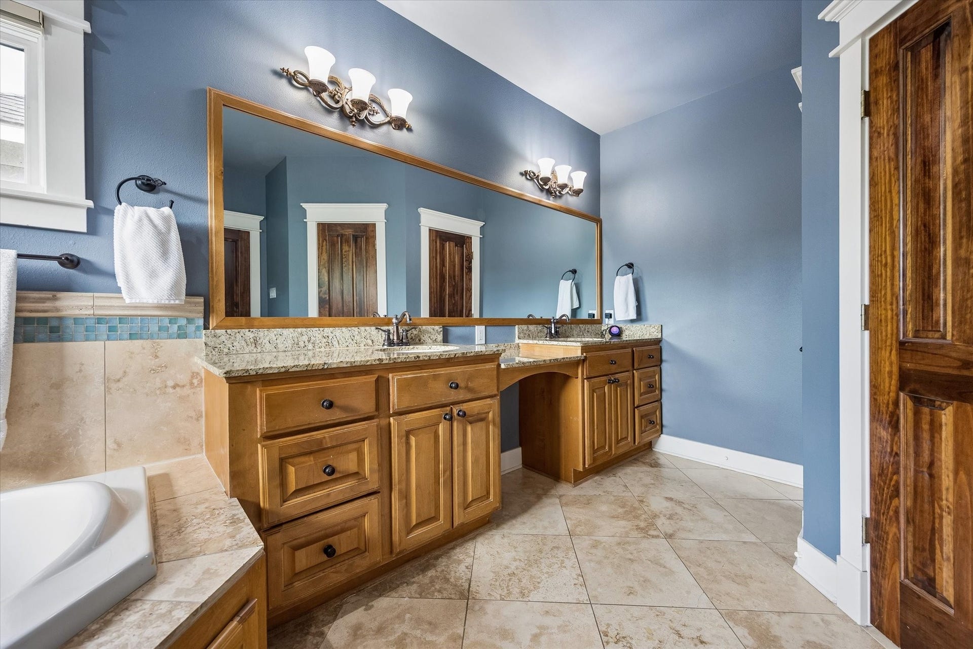 Plenty of counter space, dual sinks, knee space to sit while you primp and warm wood cabinetry make this bathroom as practical as it is inviting. Add the oversized framed mirror, stylish vanity lighting and polished finishes, and getting ready feels just a little more luxurious.