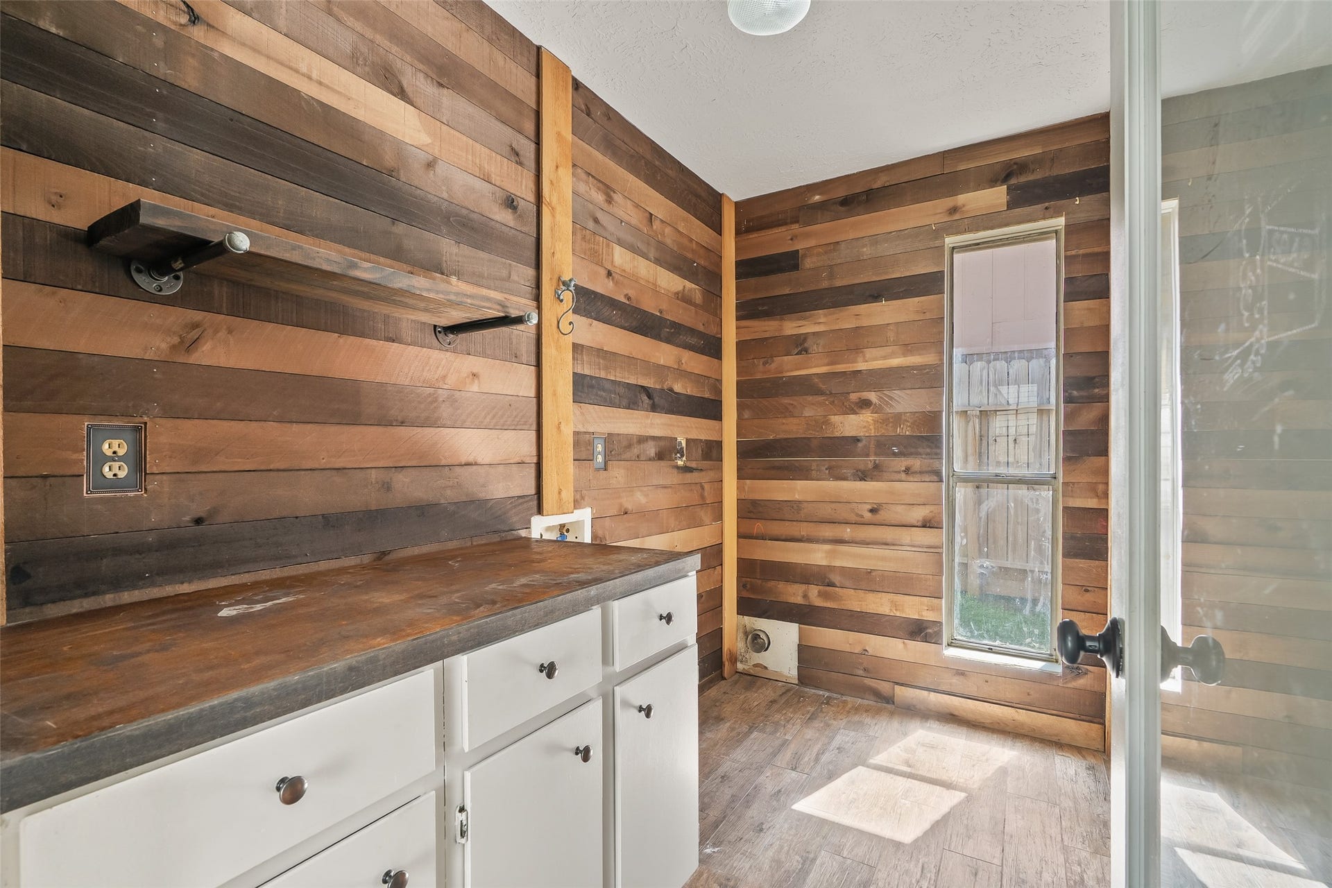 25806 Old Carriage Lane, Spring, TX 77373 Charming utility room with rustic wood paneling, featuring built-in cabinets and natural light from a tall window.