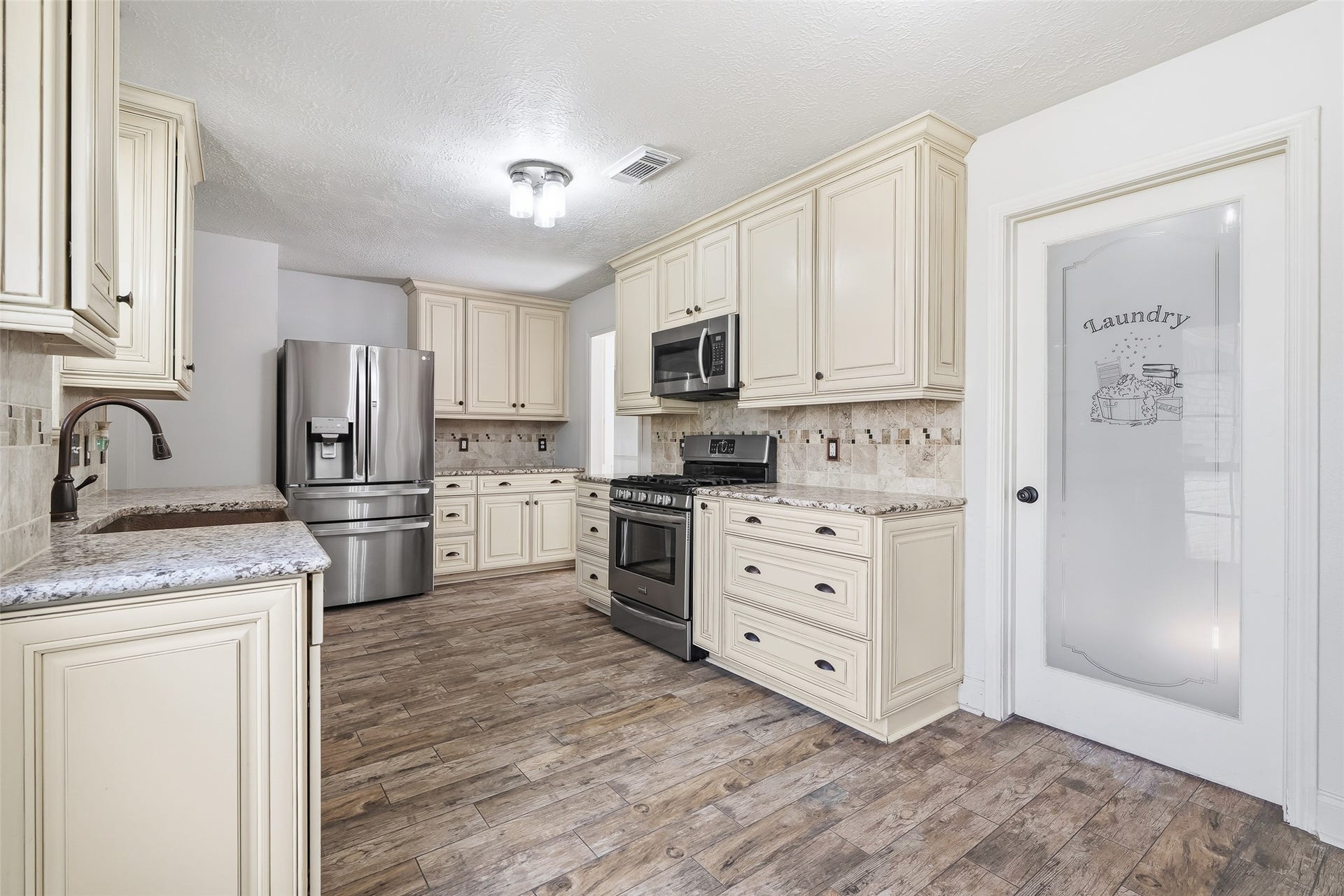 25806 Old Carriage Lane, Spring, TX 77373 Spacious kitchen with elegant cream cabinetry, stainless steel appliances, and a charming glass-paneled laundry door.