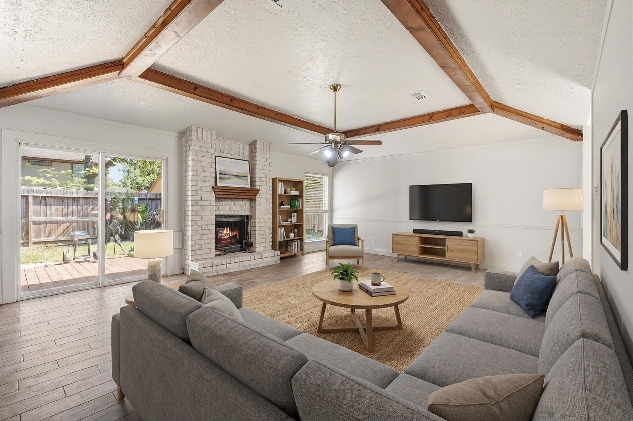 25806 Old Carriage Lane, Spring, TX 77373 Experience the perfect blend of cozy charm and modern elegance in this bright living room, featuring exposed wooden beams, a warm brick fireplace, and seamless access to the backyard. This image is AI enhanced.