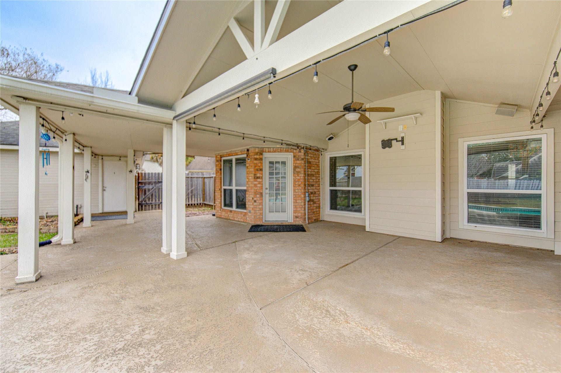 This spacious covered patio with a ceiling fan and string lights, TV wall mount, semi sheer outdoor roller shade  ideal for outdoor relaxation and entertaining.