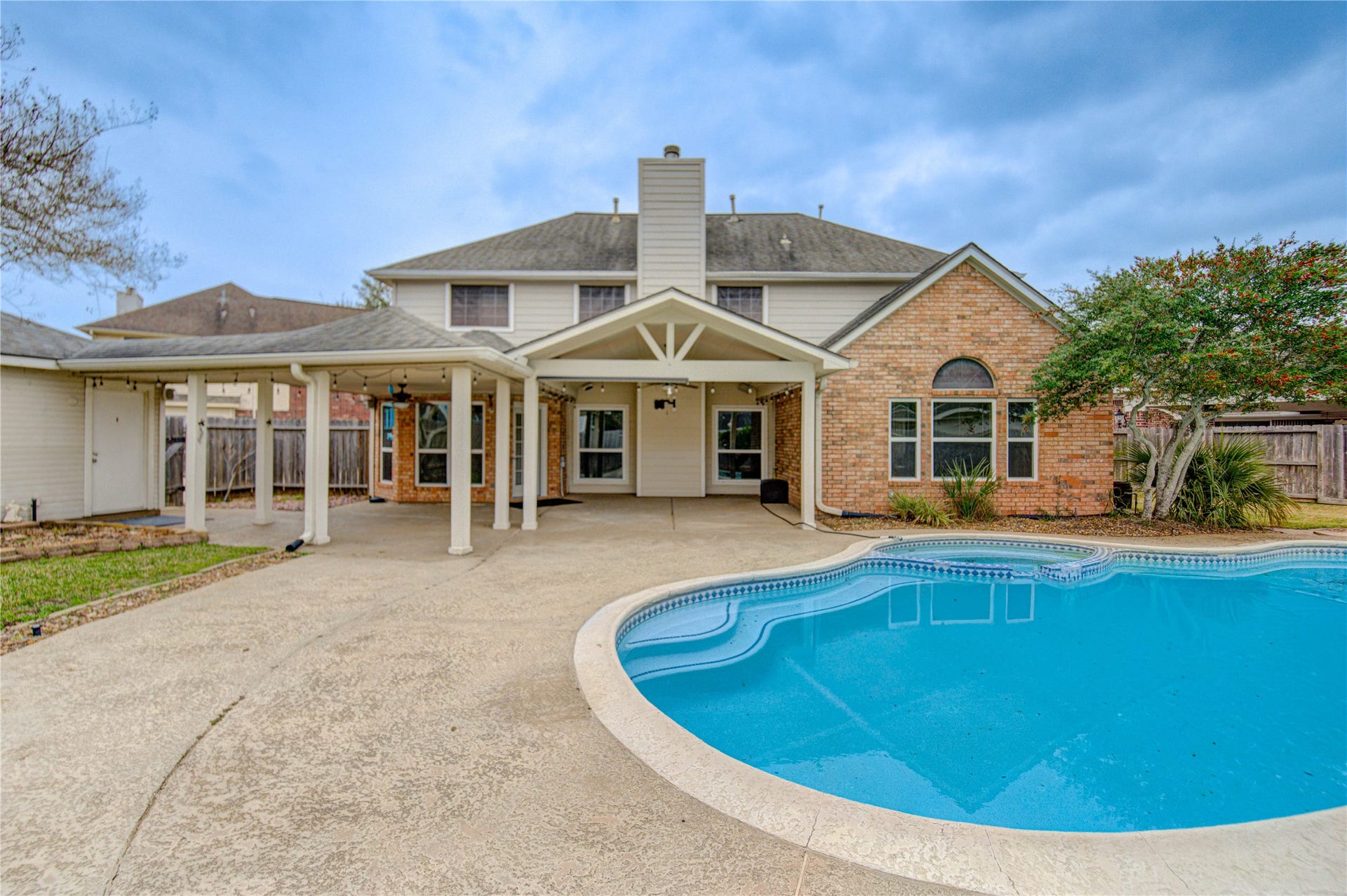 Spacious backyard featuring a well-maintained lawn, a kidney-shaped pool, and a charming brick house with a covered patio, perfect for relaxation and entertaining.