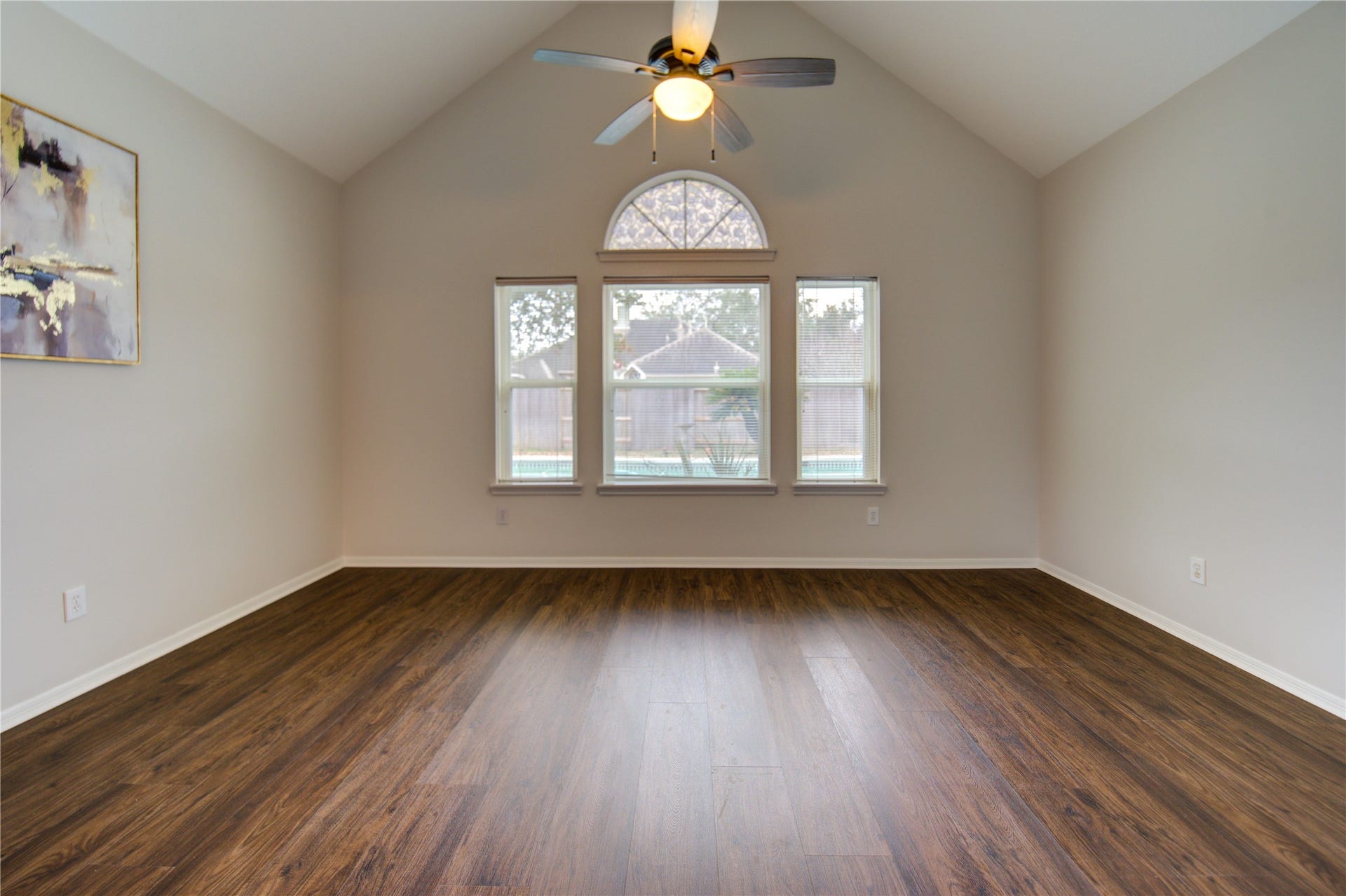 This room features a spacious layout with hardwood floors, neutral walls, and a ceiling fan. It has two doors and a piece of modern art, creating a clean and inviting space.