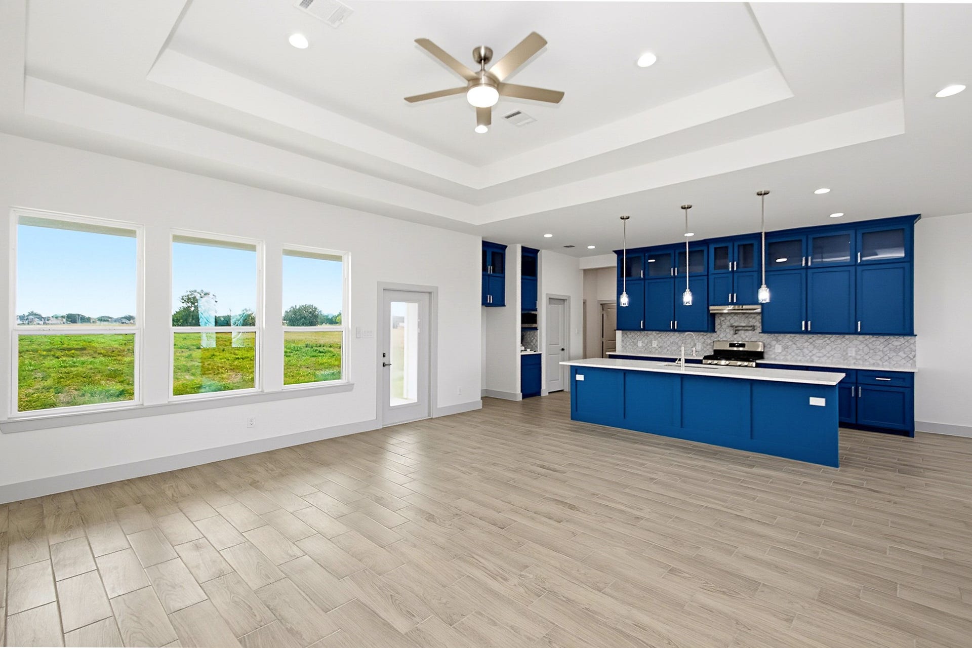 619 Longhorn Trail, Angleton, TX 77515 Spacious open-concept living area with elegant tile flooring, abundant natural light from large windows, and a striking kitchen featuring bold blue cabinetry and modern pendant lighting.