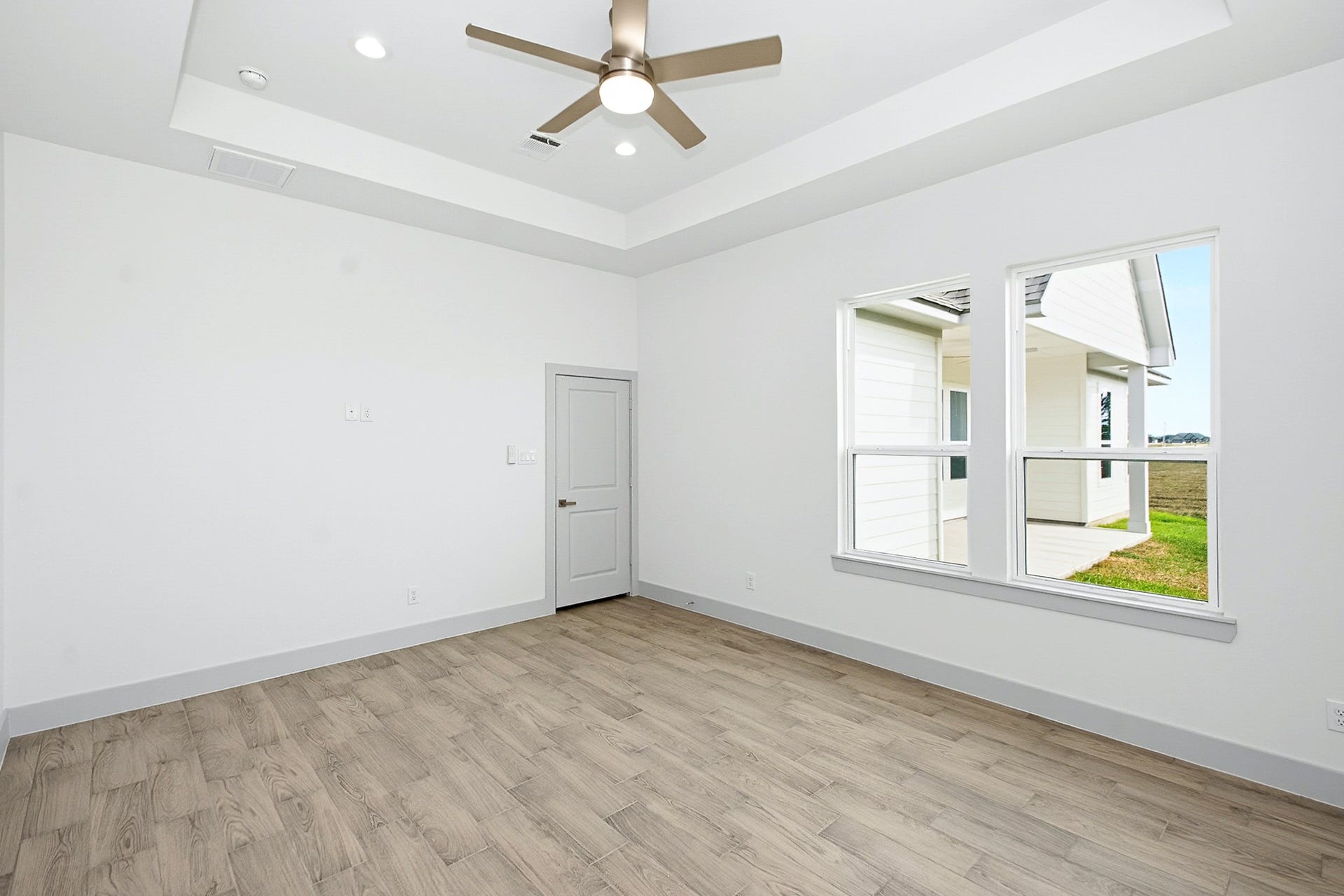 619 Longhorn Trail, Angleton, TX 77515 Bright and airy primary bedroom featuring a modern ceiling fan, wood-look tile flooring, and large windows overlooking a covered patio and expansive views.