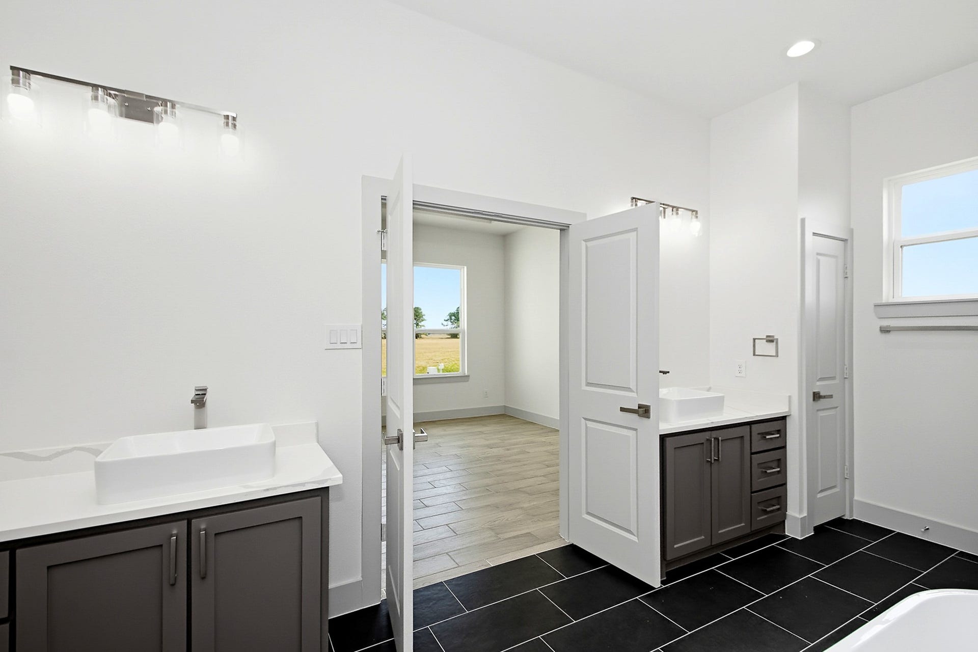 619 Longhorn Trail, Angleton, TX 77515 Spacious 16x12 primary bathroom featuring dual vanities, sleek black tile flooring, and ample natural light from large windows, offering a modern and functional design.