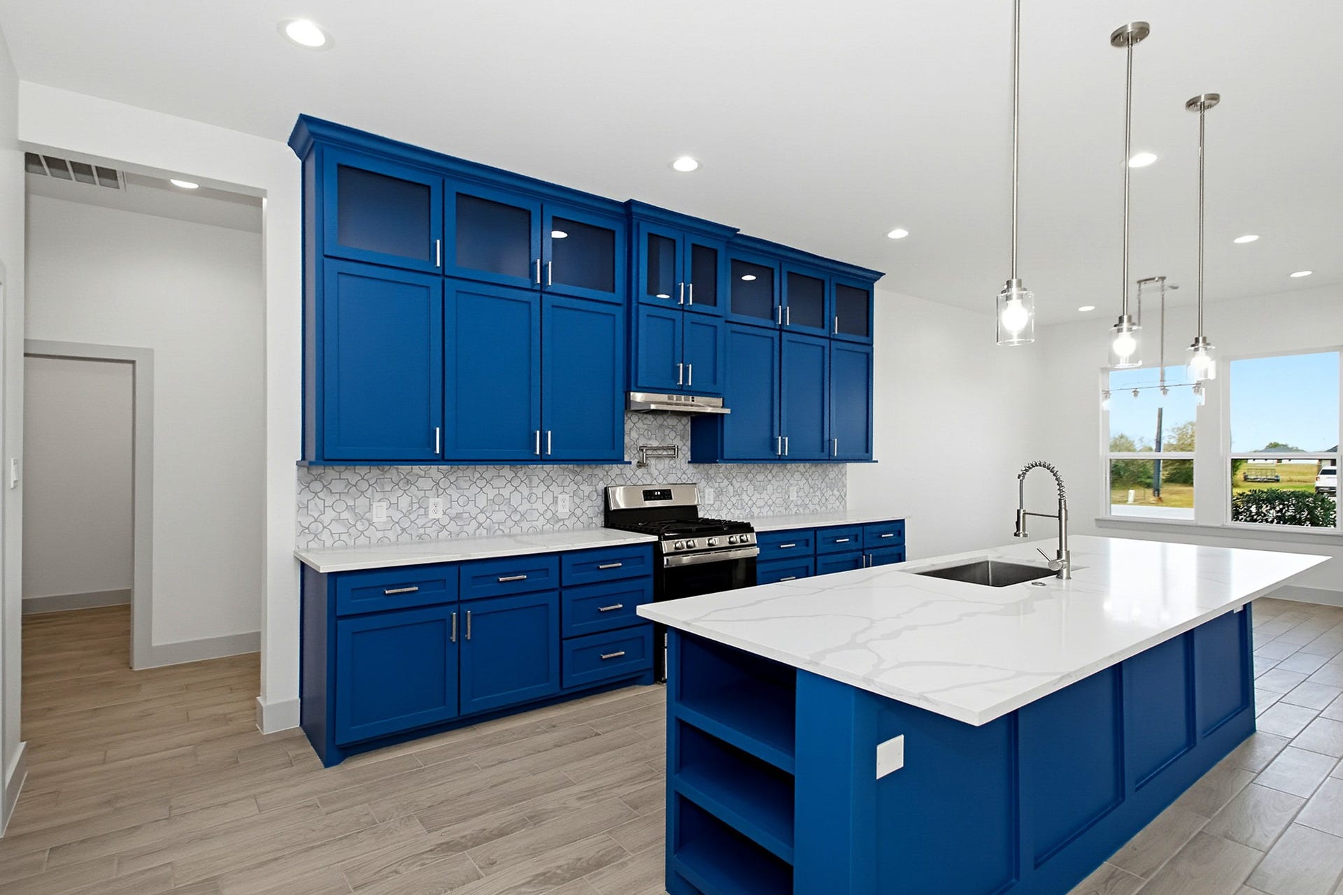 619 Longhorn Trail, Angleton, TX 77515 Stunning modern kitchen featuring bold blue cabinetry, sleek stainless steel appliances, and a spacious island with elegant pendant lighting and quartz countertops, perfect for entertaining.