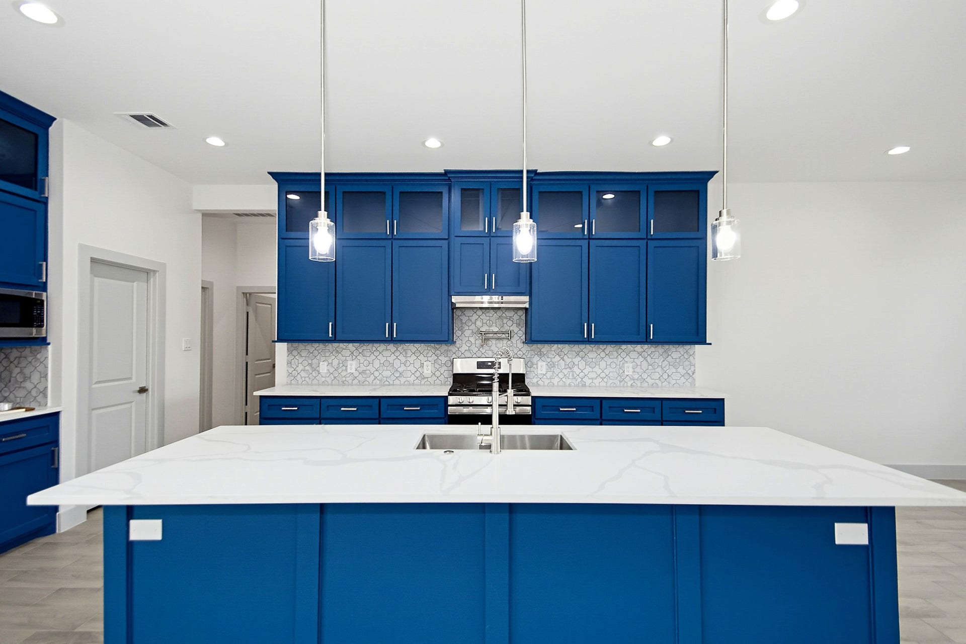 619 Longhorn Trail, Angleton, TX 77515 Stunning 19x14 kitchen with bold blue cabinetry, sleek quartz countertops, and modern pendant lighting, featuring a central island with a built-in sink.