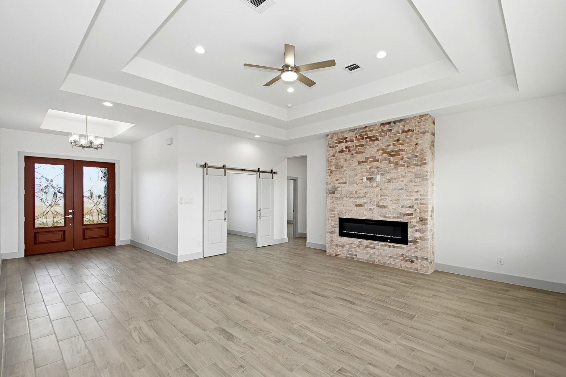 619 Longhorn Trail, Angleton, TX 77515 Elegant 19x 16 living area featuring a striking brick accent wall with a modern fireplace, complemented by stylish wood-look tile flooring and a chic coffered ceiling with recessed lighting.