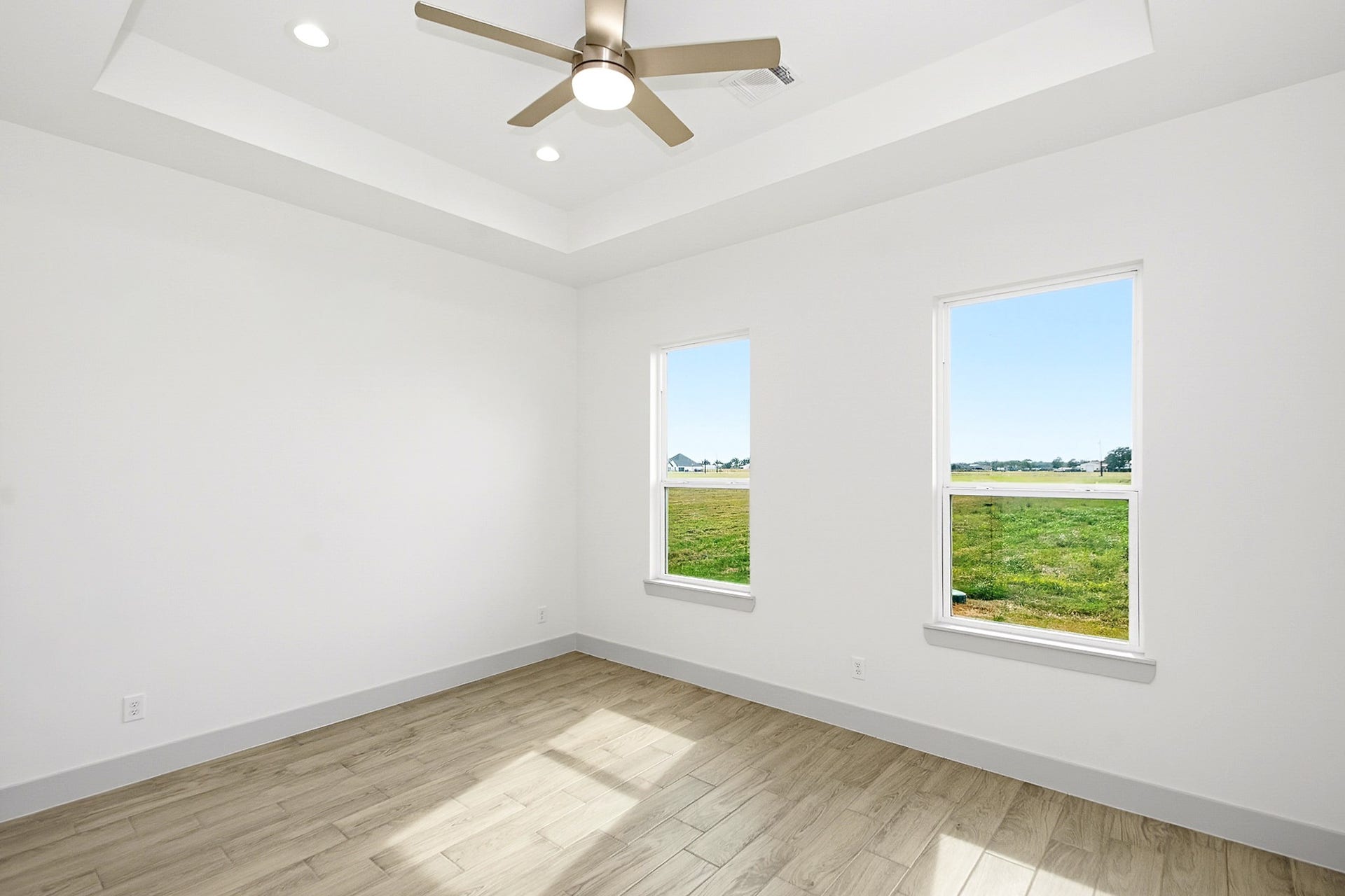 619 Longhorn Trail, Angleton, TX 77515 Bright 14.5x12 third bedroom with large windows offering scenic views, elegant tile flooring, and a modern ceiling fan set in a tray ceiling.