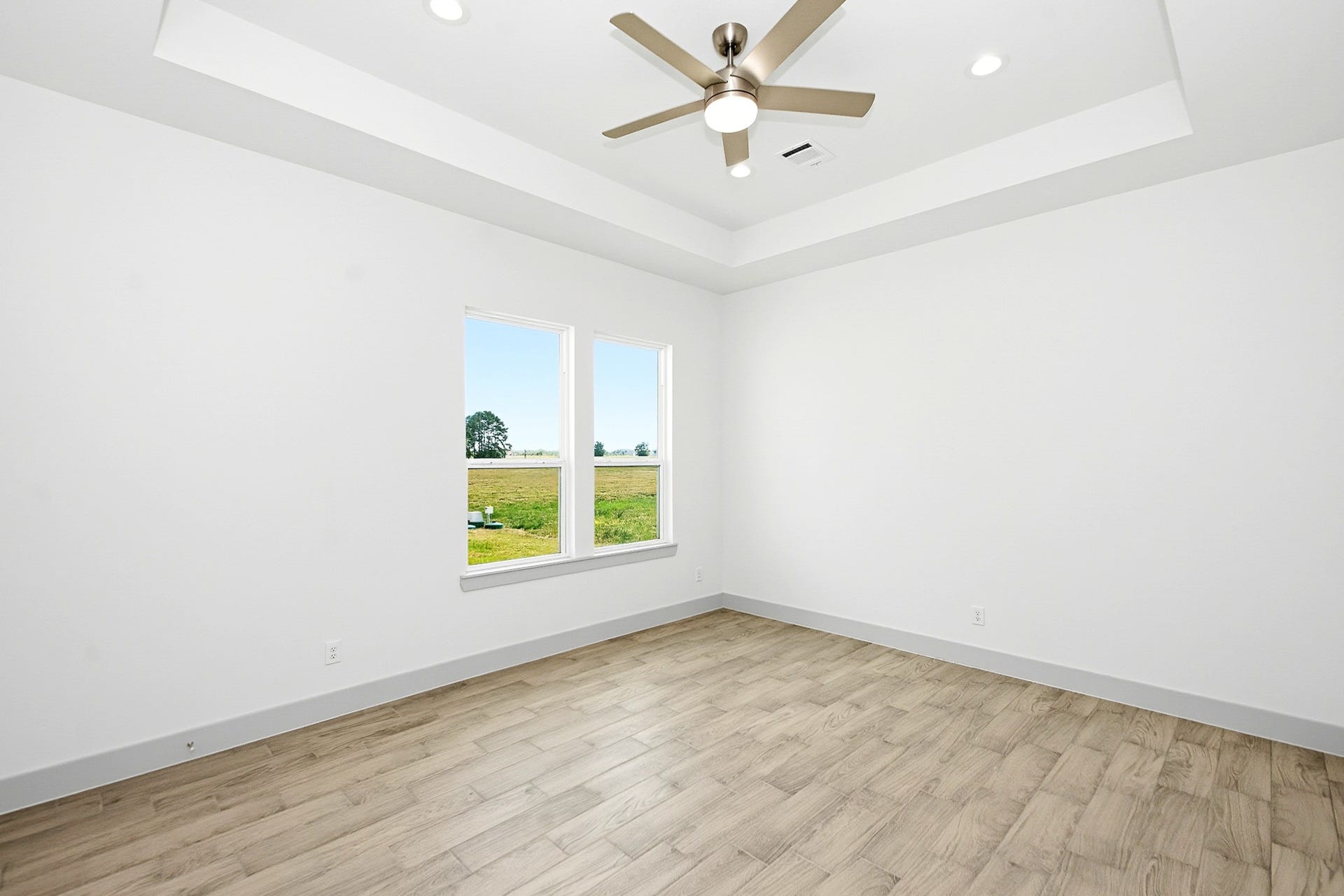 619 Longhorn Trail, Angleton, TX 77515 Bright and airy 16x13 Primary bedroom featuring a modern ceiling fan, elegant tray ceiling, and large windows offering scenic views.